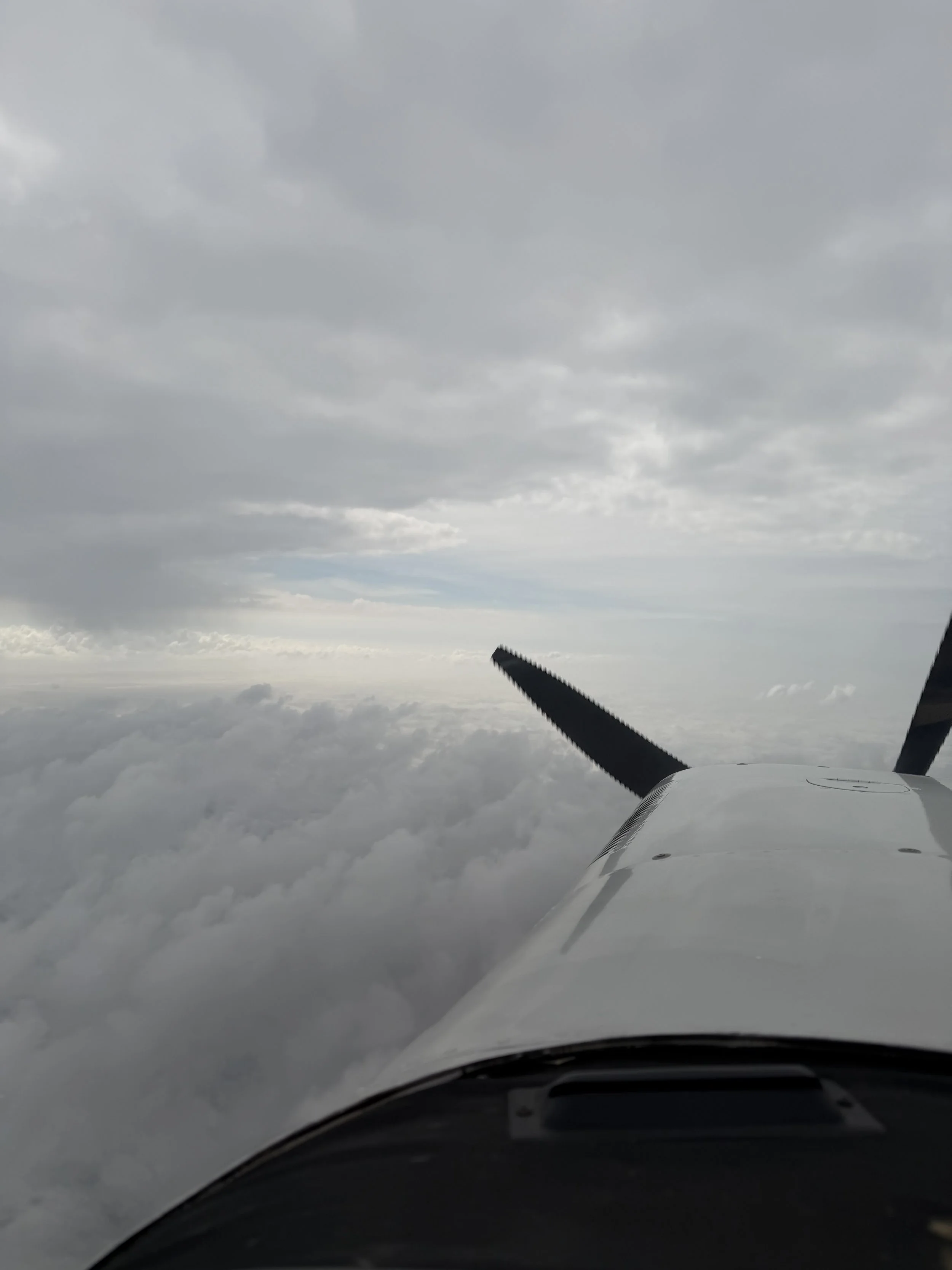 View from inside a small airplane flying above the clouds with a cloudy sky.