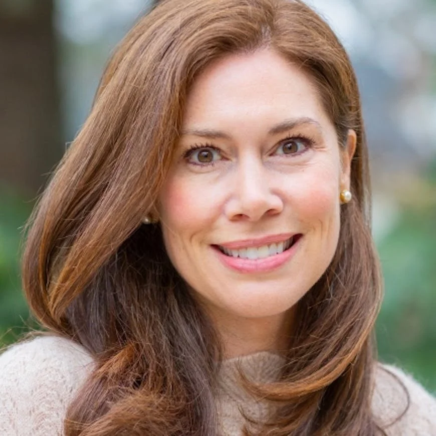Author Caroline Langerman. A woman with long reddish-brown hair smiling outdoors with greenery in the background.