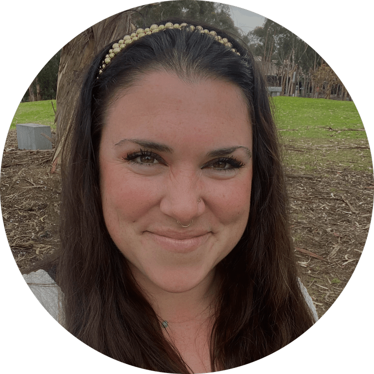 Smiling woman with long dark hair, wearing a pearl headband and a nose piercing, outdoors with trees and grass in the background.