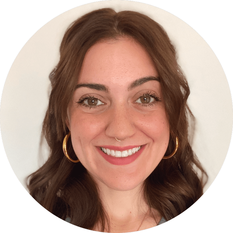 Close-up of a young woman with brown hair, hoop earrings, a septum piercing, smiling face, light makeup, in front of a white background.