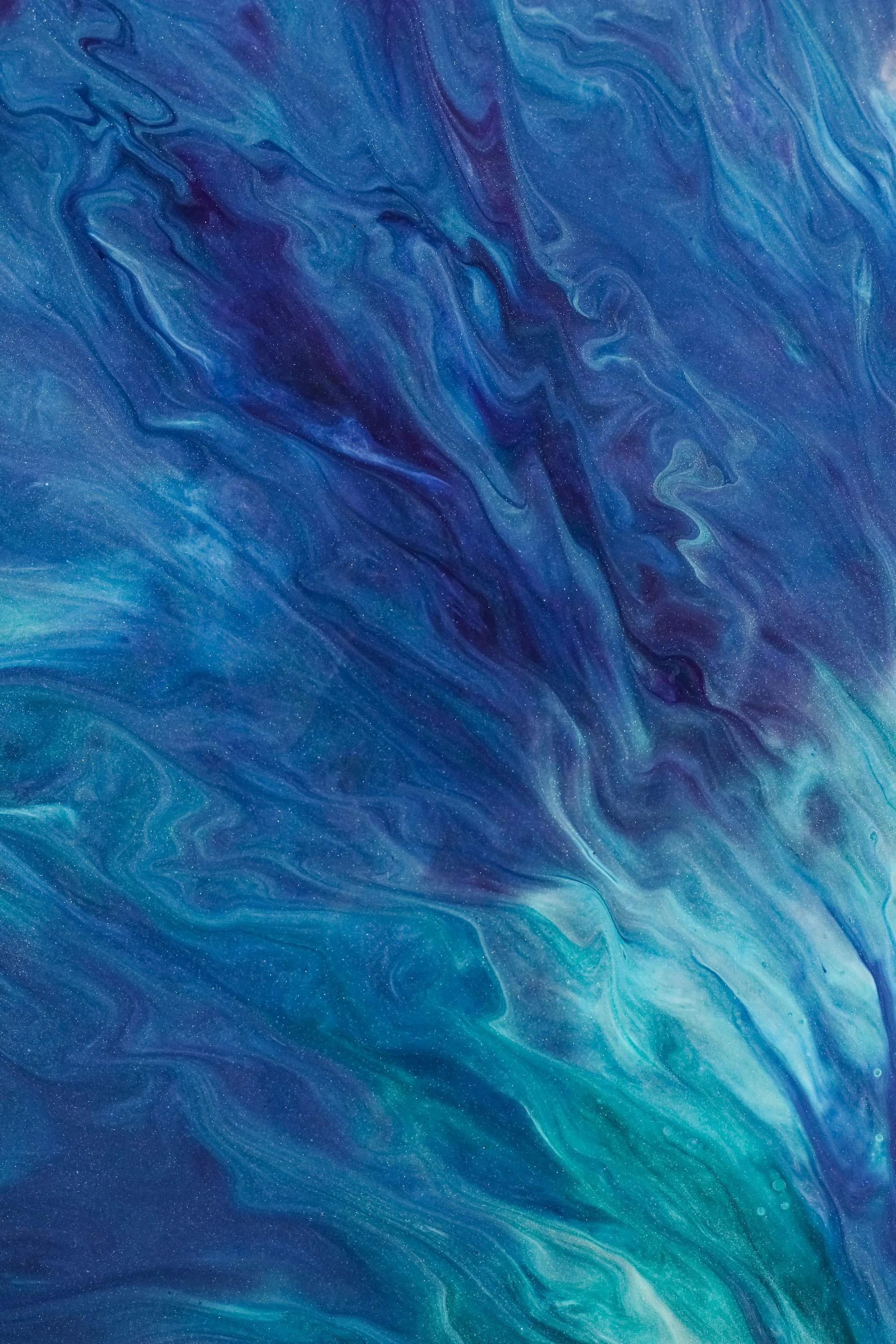 Abstract blue and teal swirling patterns resembling a galaxy or fluid motion with tiny glittering specks scattered throughout.