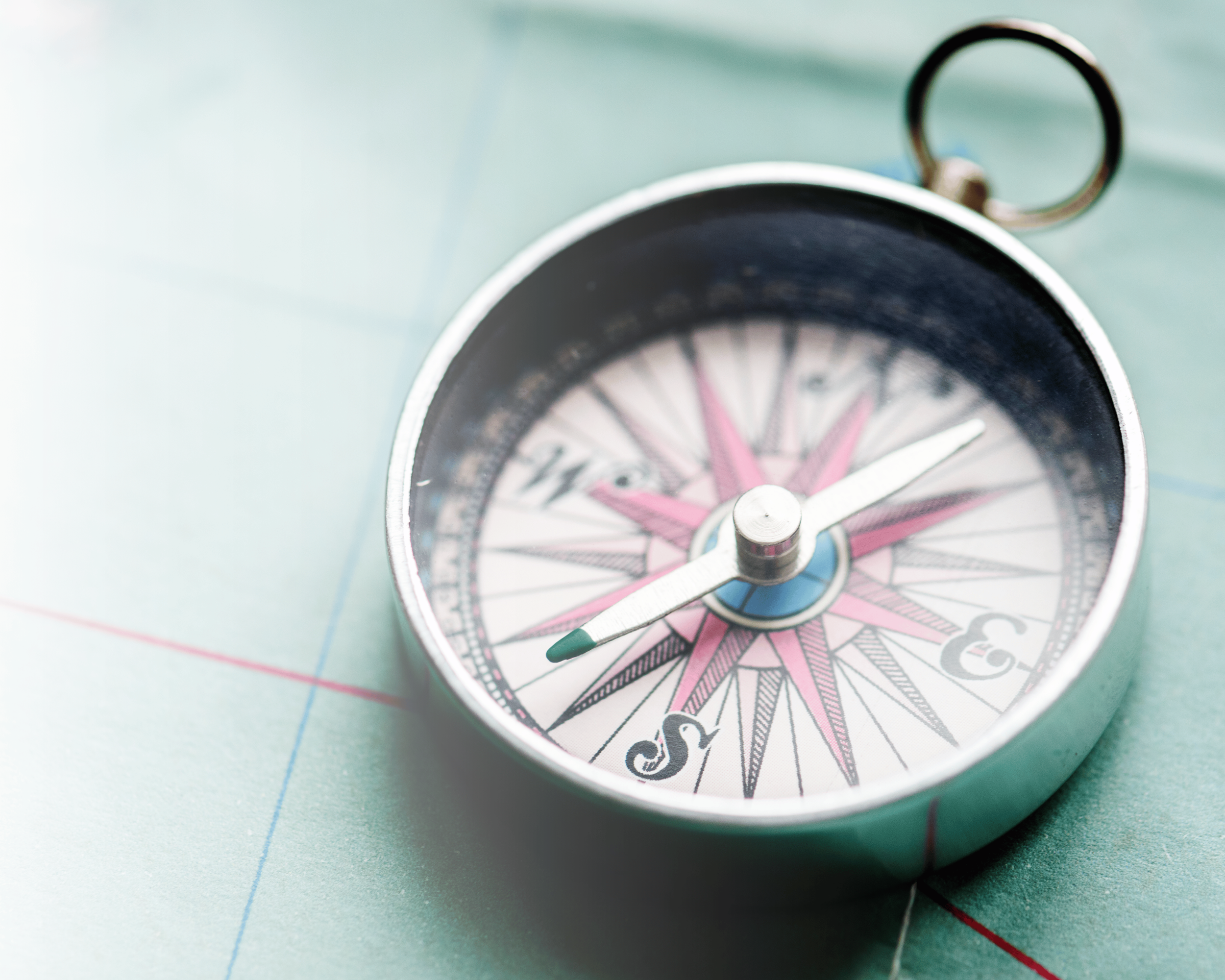 Close-up of a round compass with a pink and black design on a light green surface.