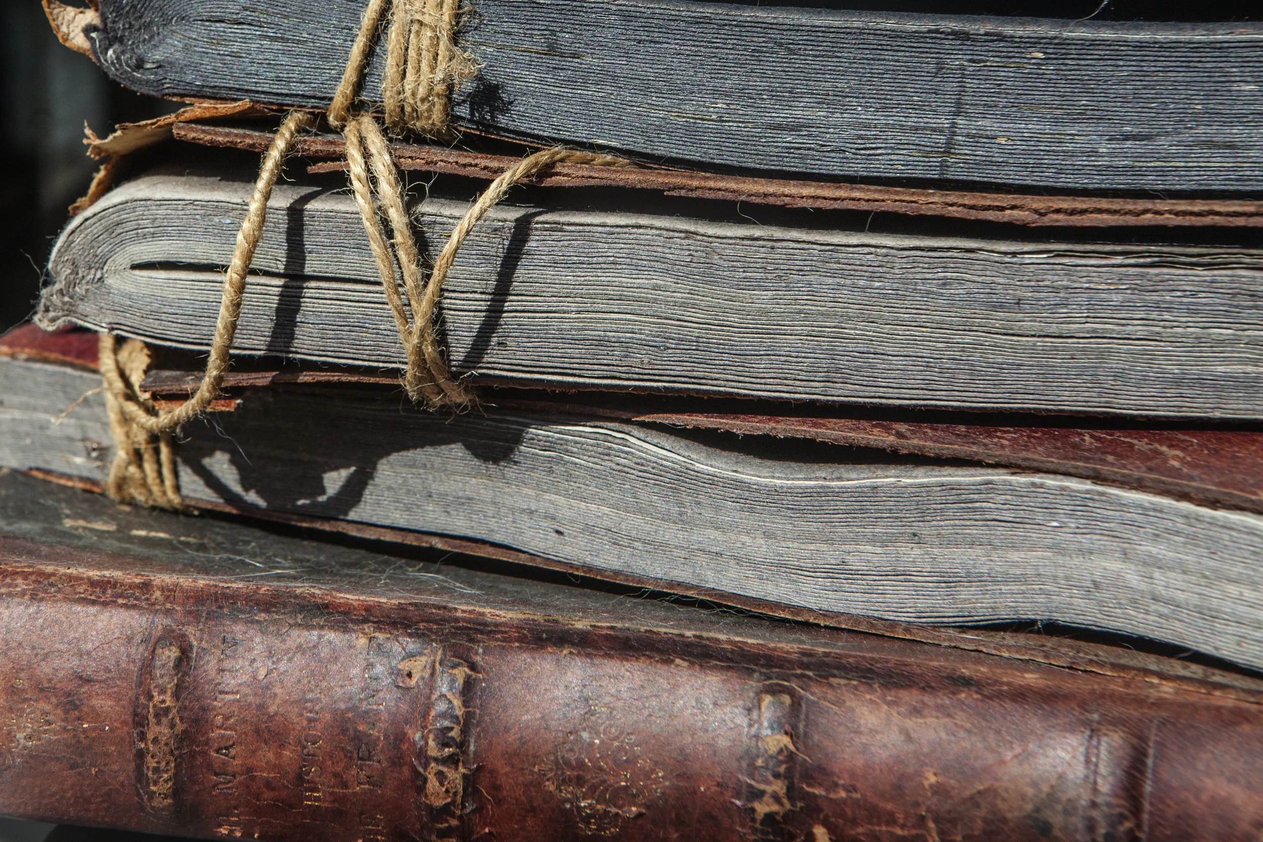 Close-up image of a weathered stack of old books tied with a rough rope, placed on a rusted metal surface.