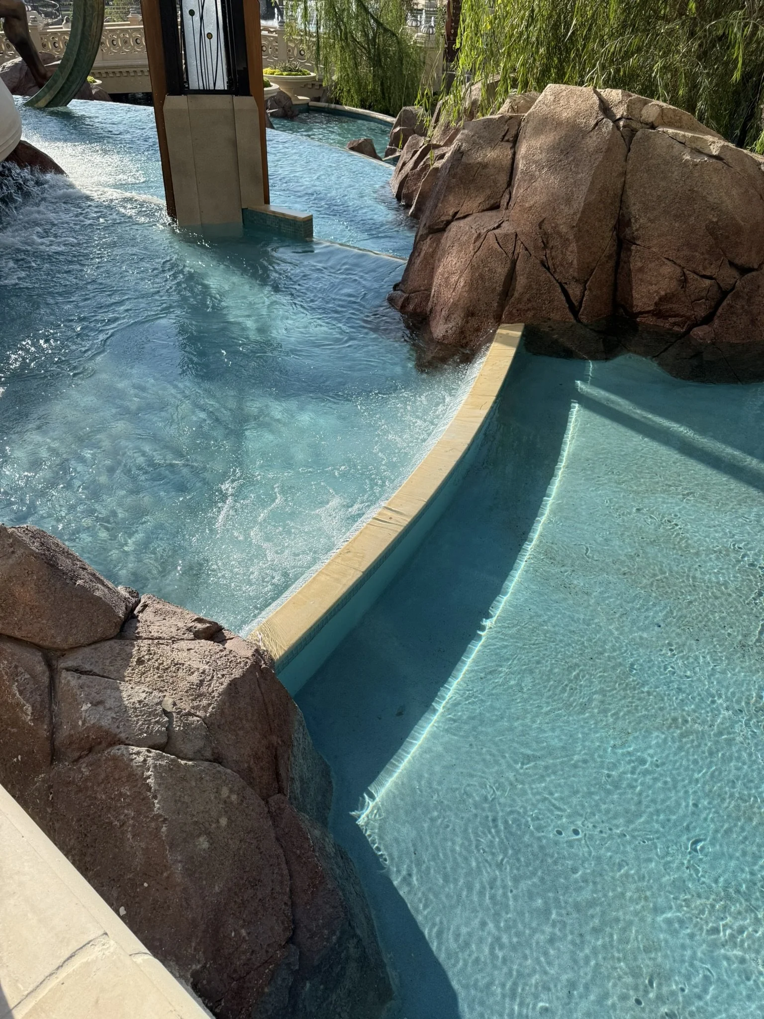 A section of a lazy river with natural rock decorations and water flowing over the edge, likely at a water park or resort.