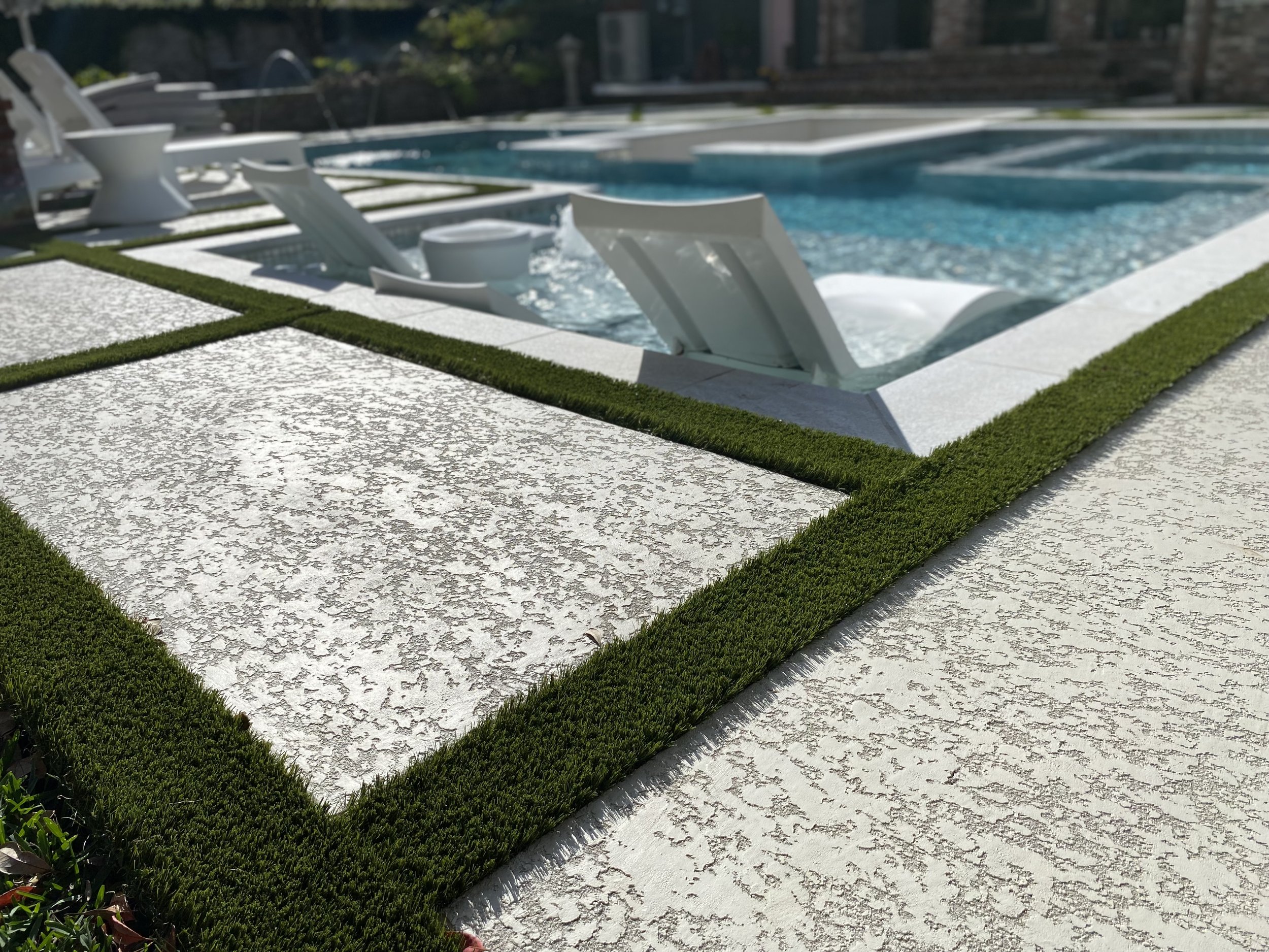 Stone steps leading up to swimming pool with chairs in the water. resurfaces patio deck with turf between the pavers.