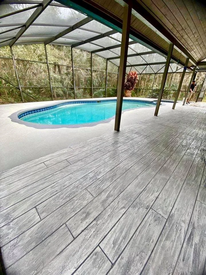 Indoor pool enclosed with a screened structure and surrounded by a wooden deck, with a person standing in the background.