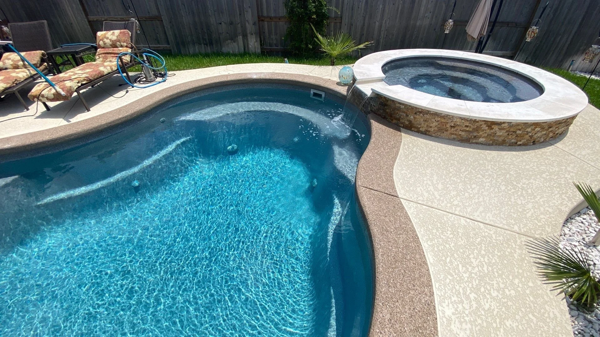 Backyard pool area with a swimming pool, hot tub, lounge chairs, and a wooden fence.
