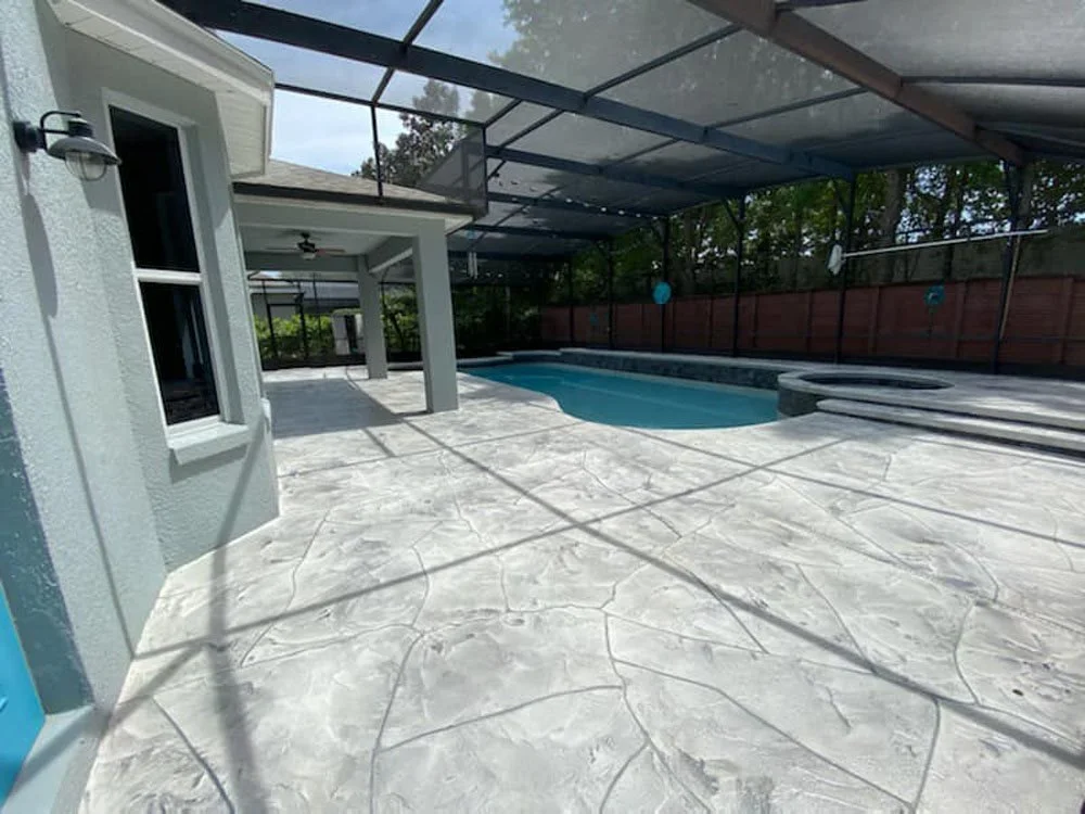 Backyard with a swimming pool, covered patio, and screened enclosure, featuring concrete stamped flooring and outdoor lighting.