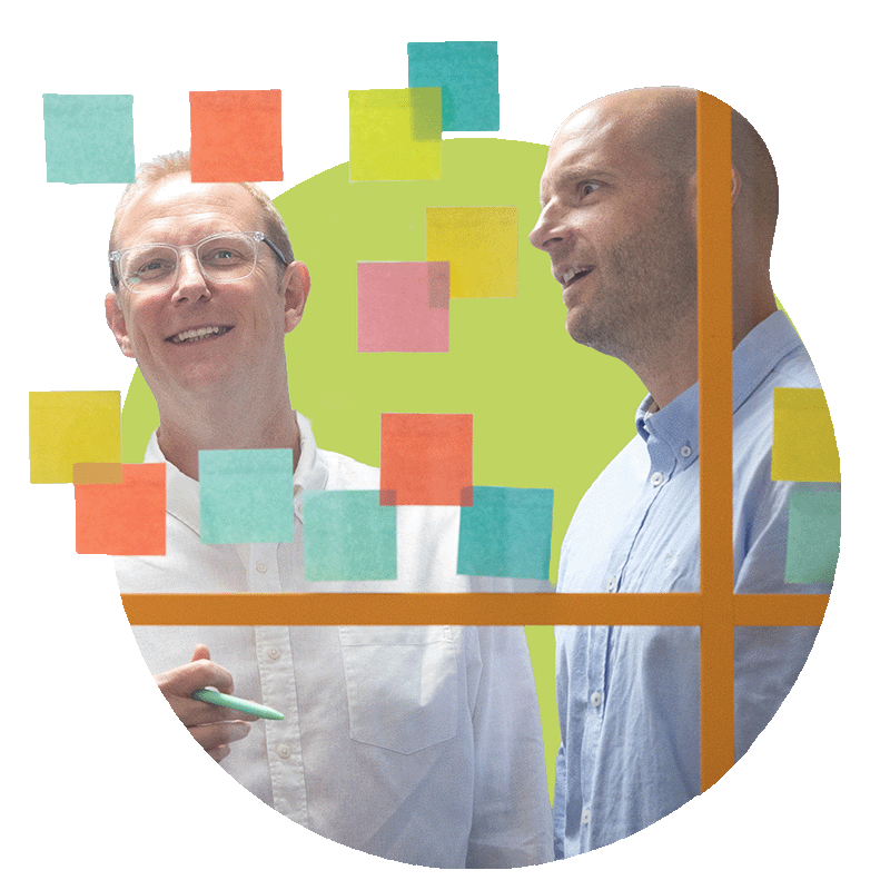 Two men engaging in a discussion behind a glass board covered with colourful sticky notes.