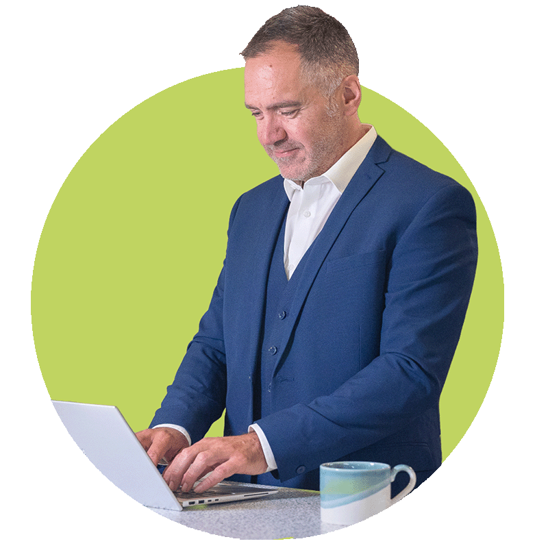 A man in a blue suit working on a laptop at a desk with a coffee mug, set against a circular light green background.