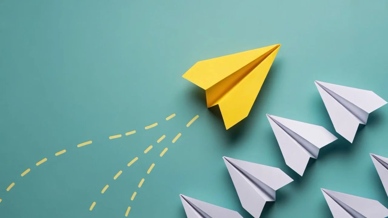 A yellow paper airplane with dotted lines beneath it indicating flight, flying past white paper airplanes on a green background.