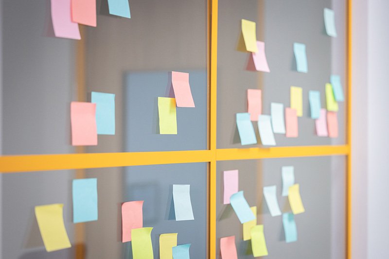 A glass wall or window with colourful sticky notes attached in a grid pattern, with a yellow frame dividing sections.