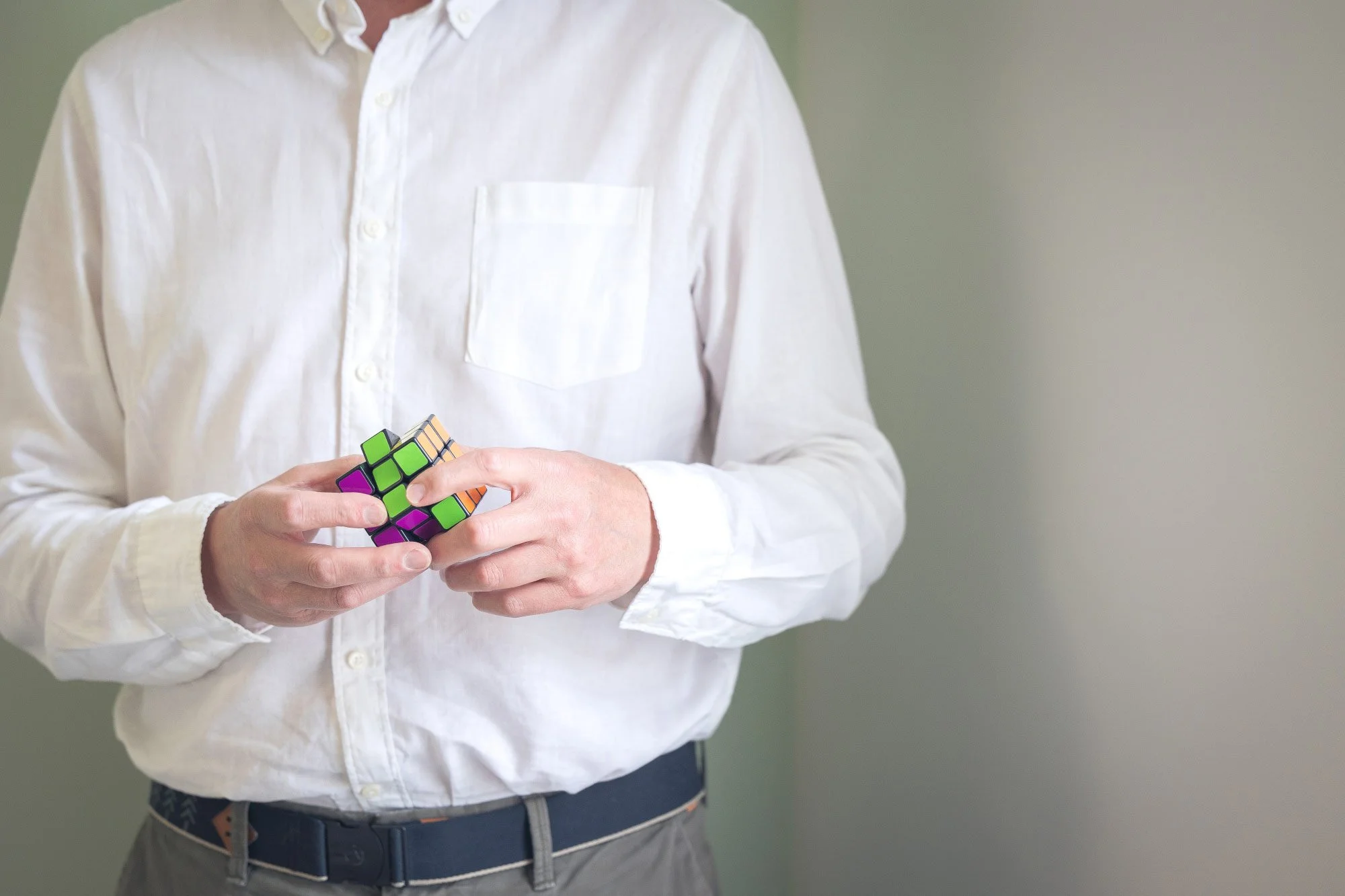 Person in a white button-up shirt holding a Rubik's Cube against a plain background.
