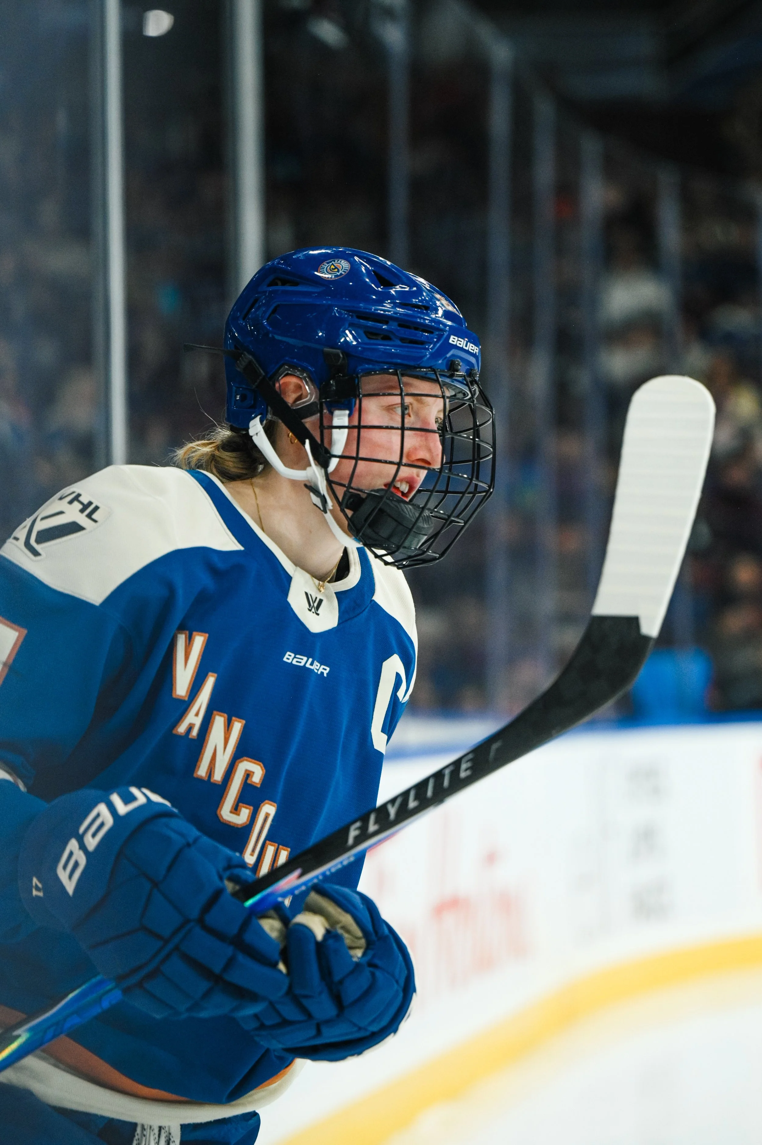 An ice hockey player wearing a blue jersey with orange accents and a blue helmet on the ice rink.
