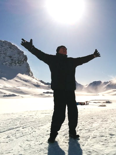 Person in winter clothing standing in snow with arms outstretched under the sun in a snowy landscape