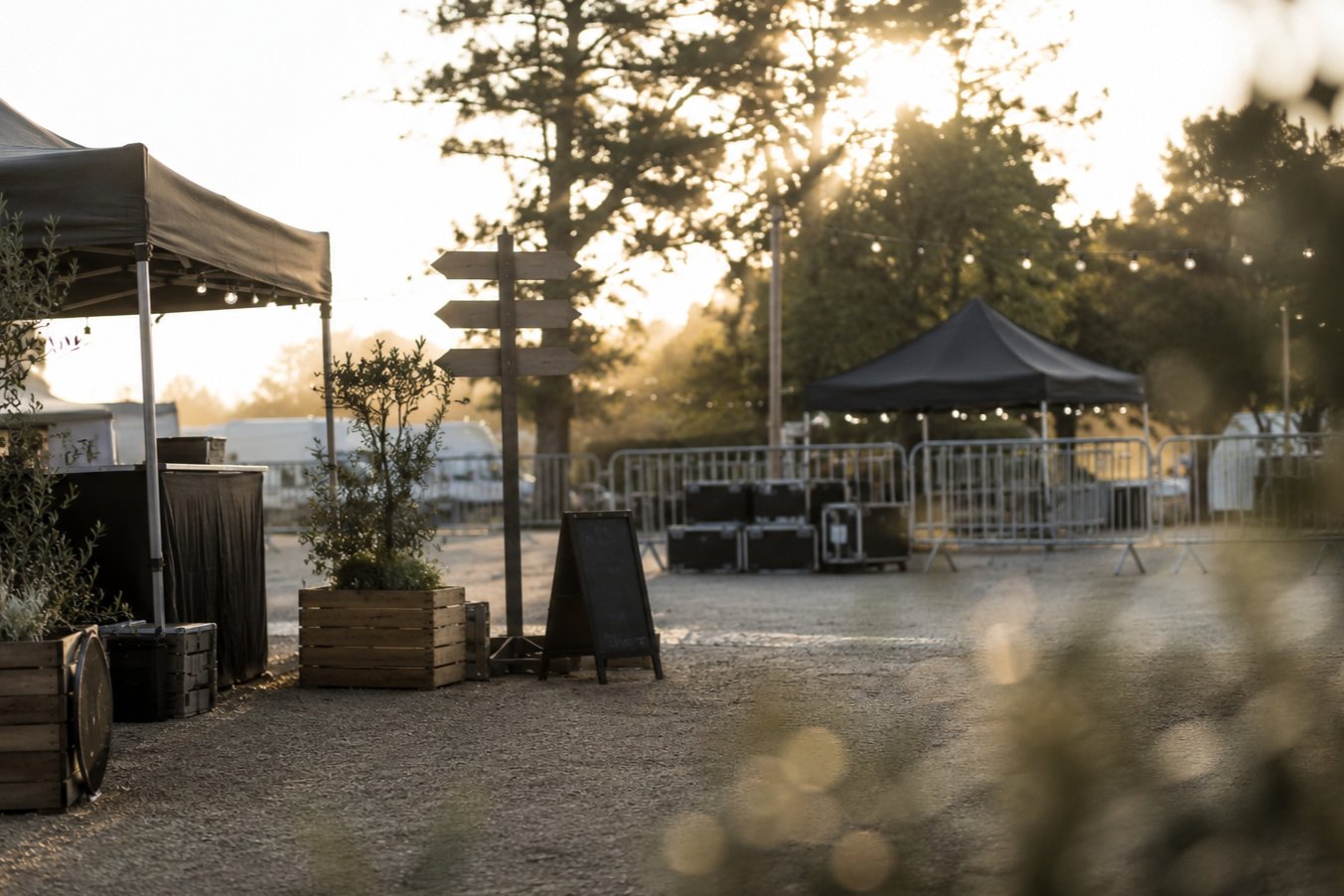 Outdoor event setup with tents, barriers, and string lights at sunrise.