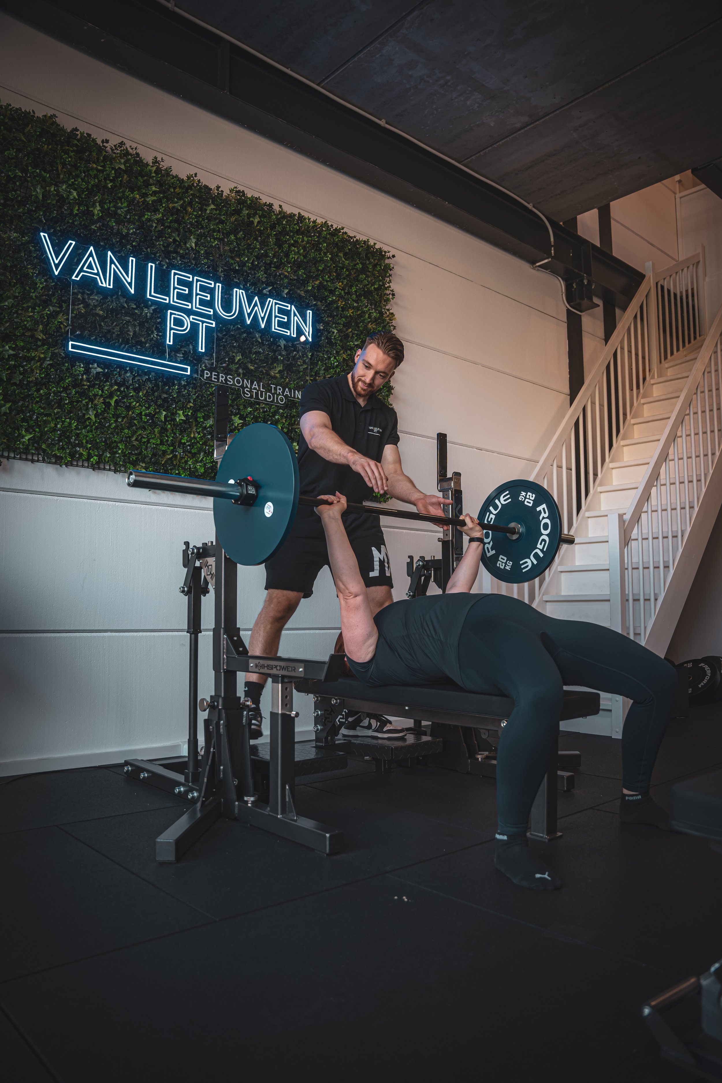 Fitness trainer helpt persoon met gewichtheffen in gym, van Leeuwen PT Personal Train Studio. Zoetermeer