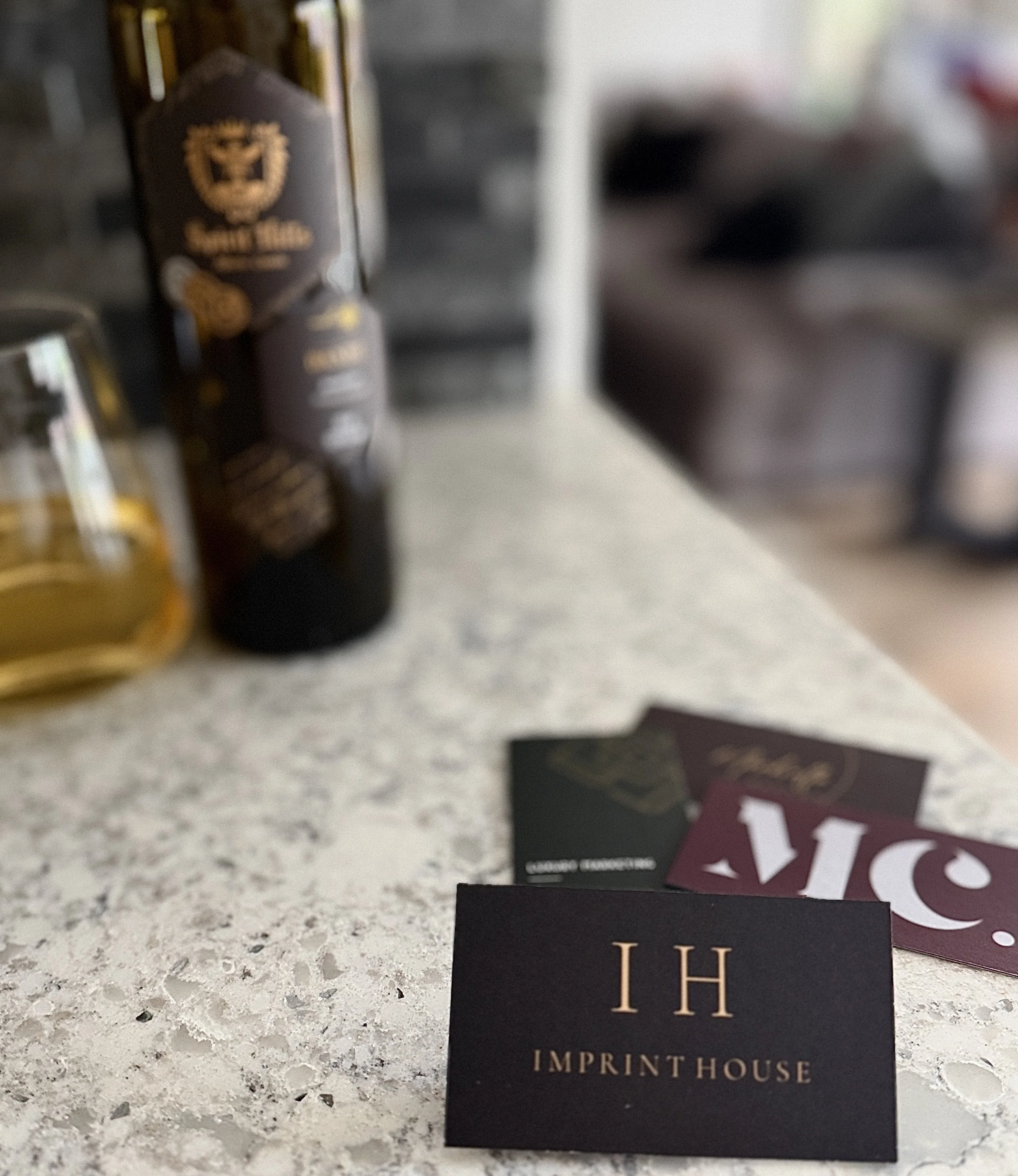 Luxury black and gold Imprint House business card displayed beside wine in a luxury editorial setting.
