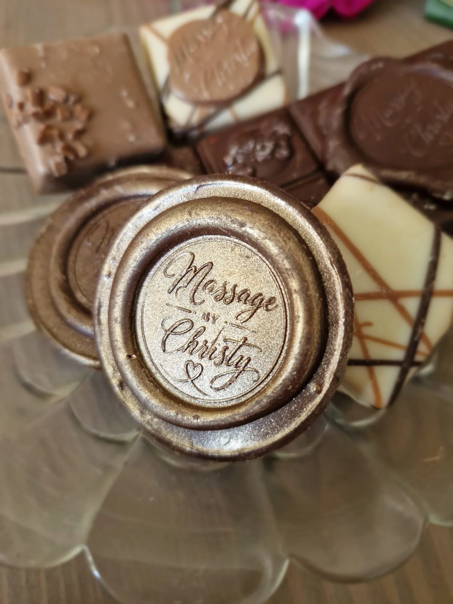Close-up of assorted chocolates with a gold embossed lid reading 'Message in a Choc' in a glass container.