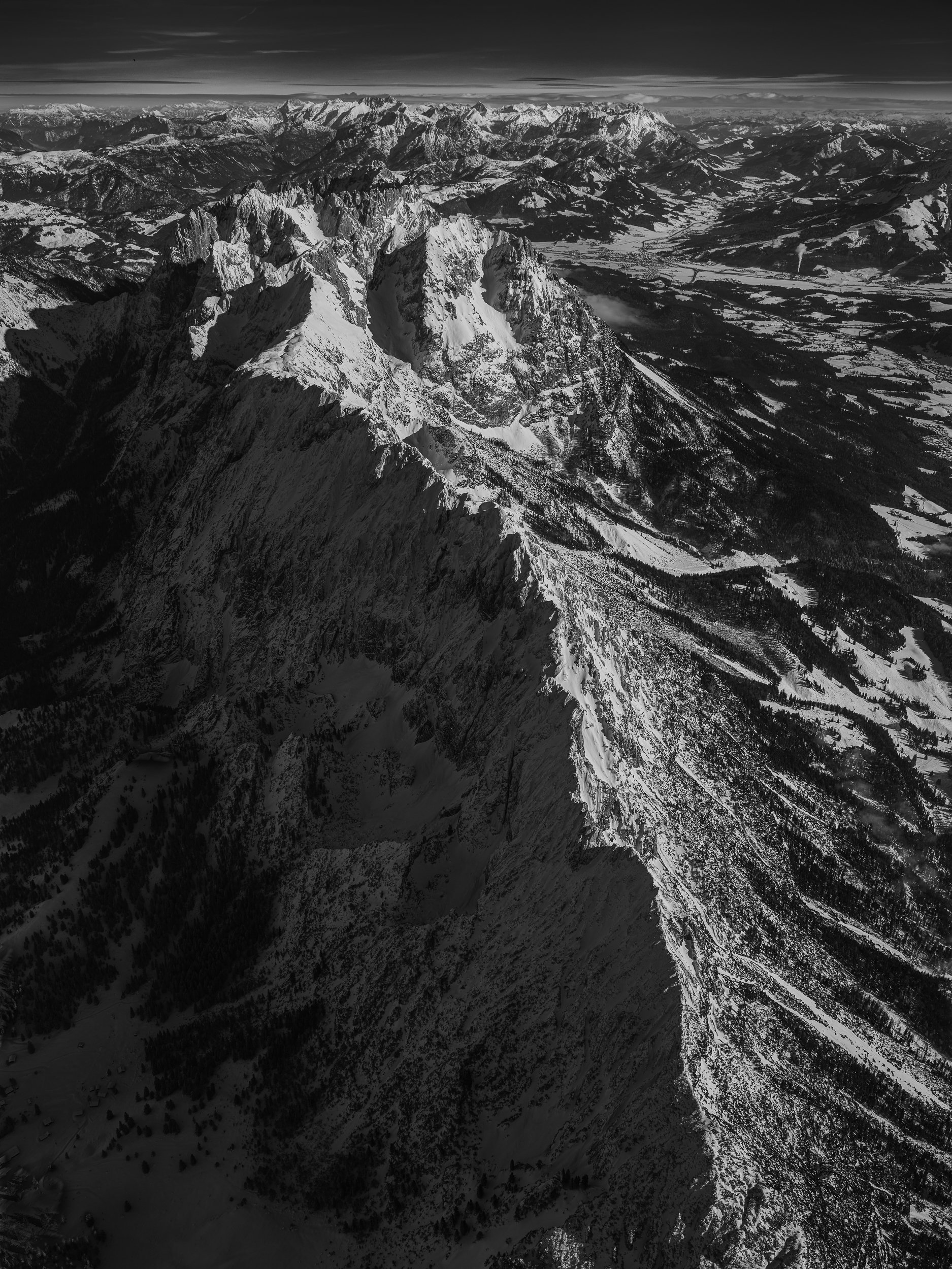 Schneebedeckte Berggipfel und Täler in einer alpinen Landschaft, aufgenommen aus der Luft in Schwarz-Weiß.