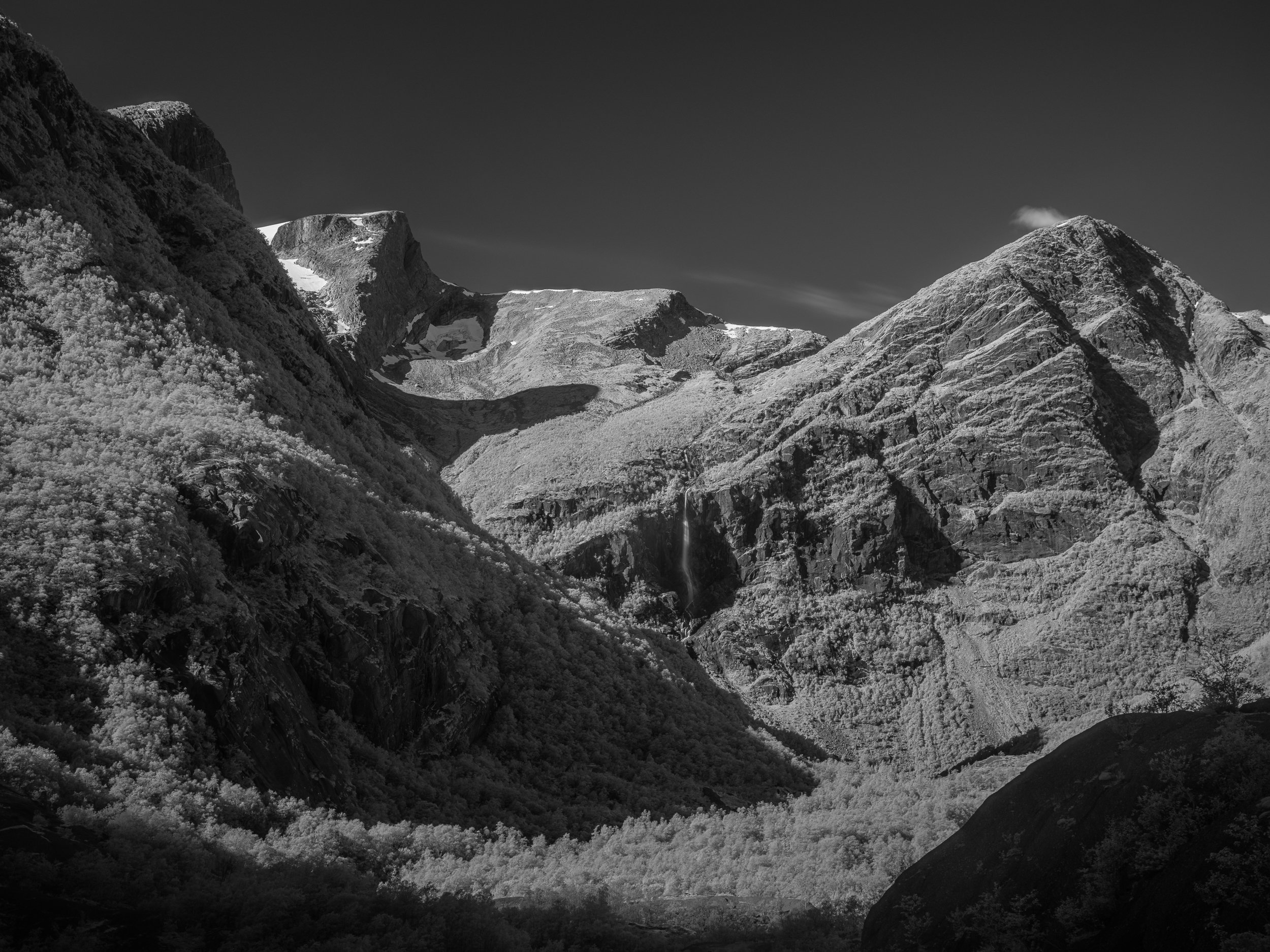 Schneebedeckte Berggipfel und ein Wasserfall im Tal unter einem klaren Himmel.