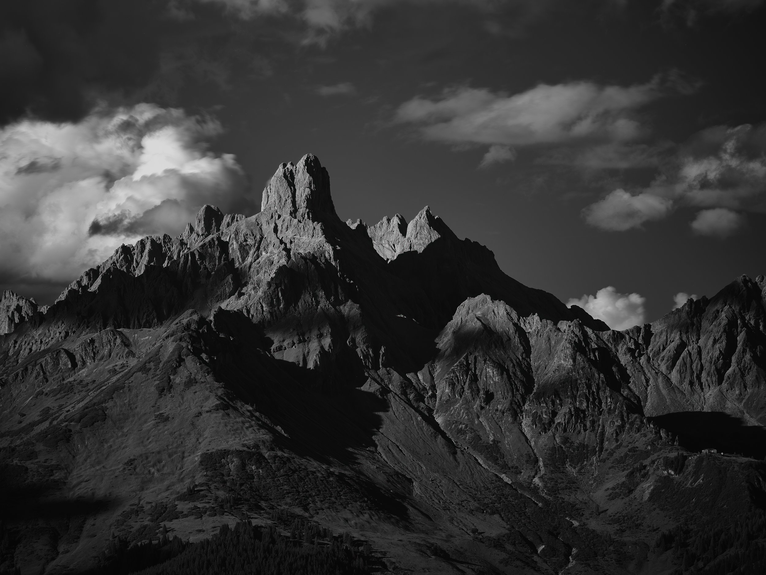 Schwarzes und weißes Berglandschaftsbild mit schroffen Gipfeln und Wolken am Himmel.