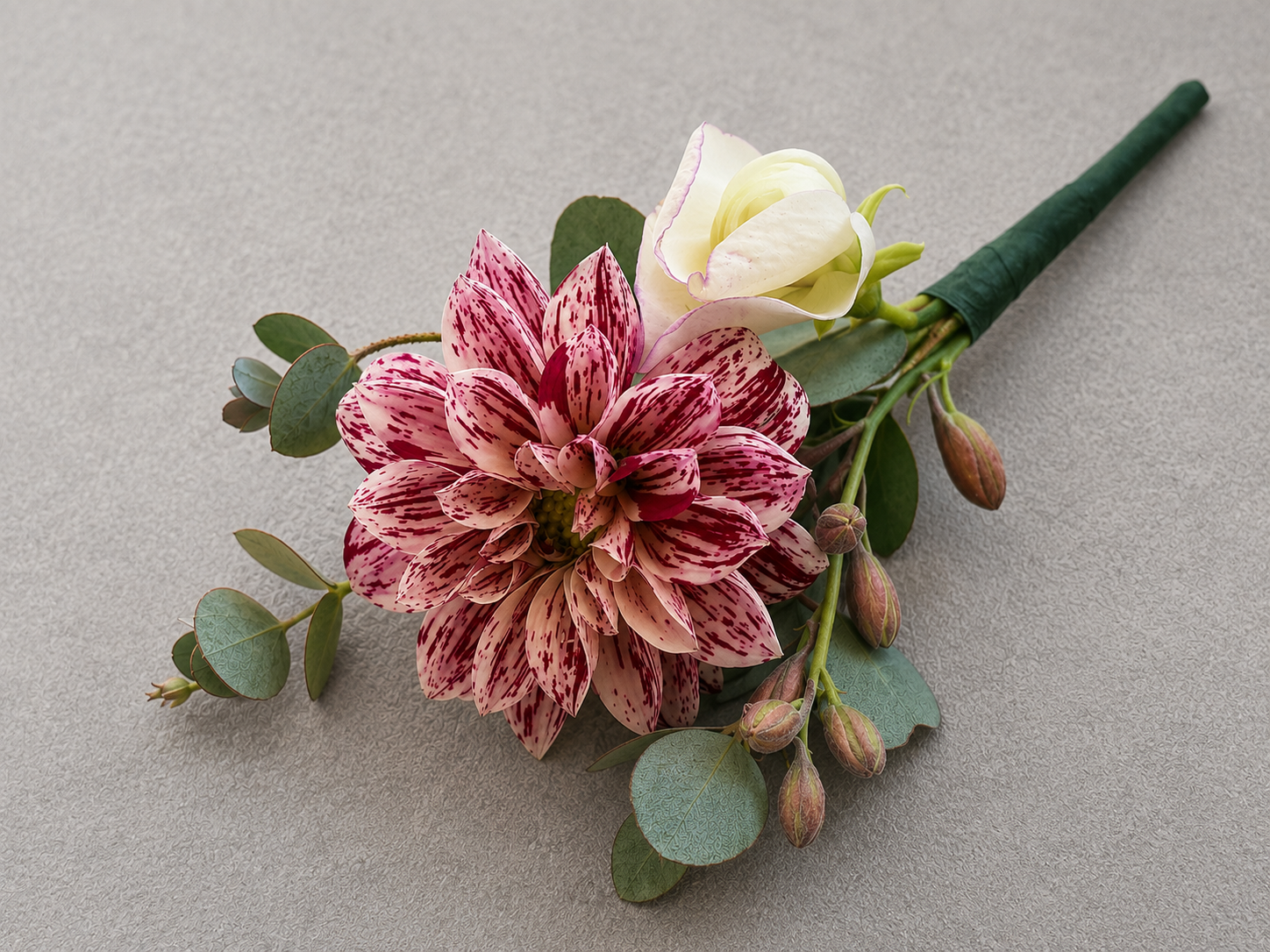 Bouquet with a pink and white variegated dahlia, a white calla lily, eucalyptus leaves, and small flower buds on a neutral background.