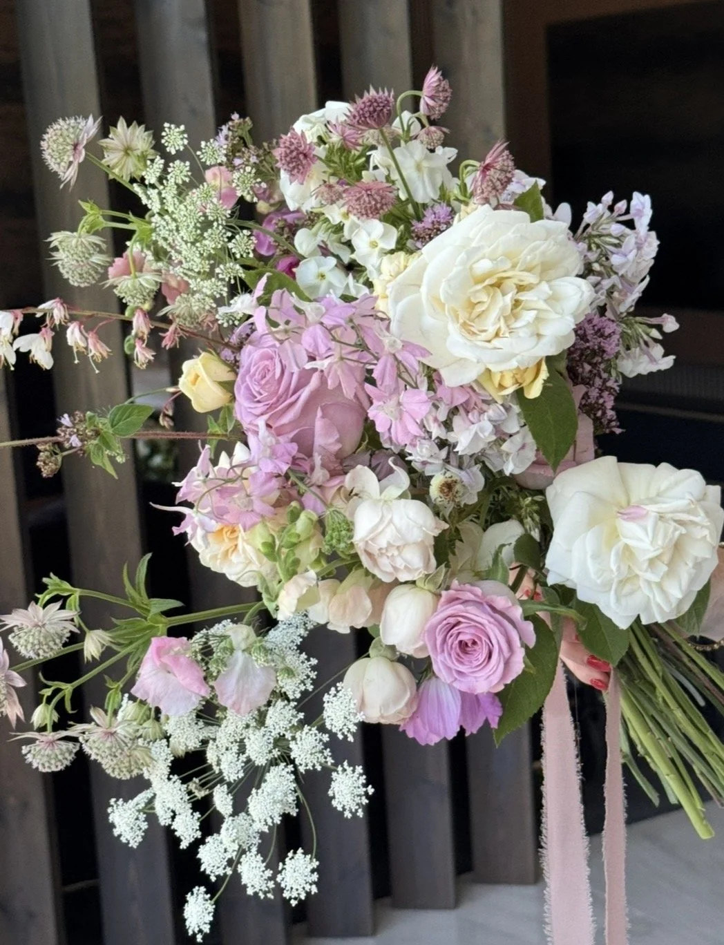 A bouquet of pink, white, and purple flowers, including roses and other blooms, tied with a pink ribbon.