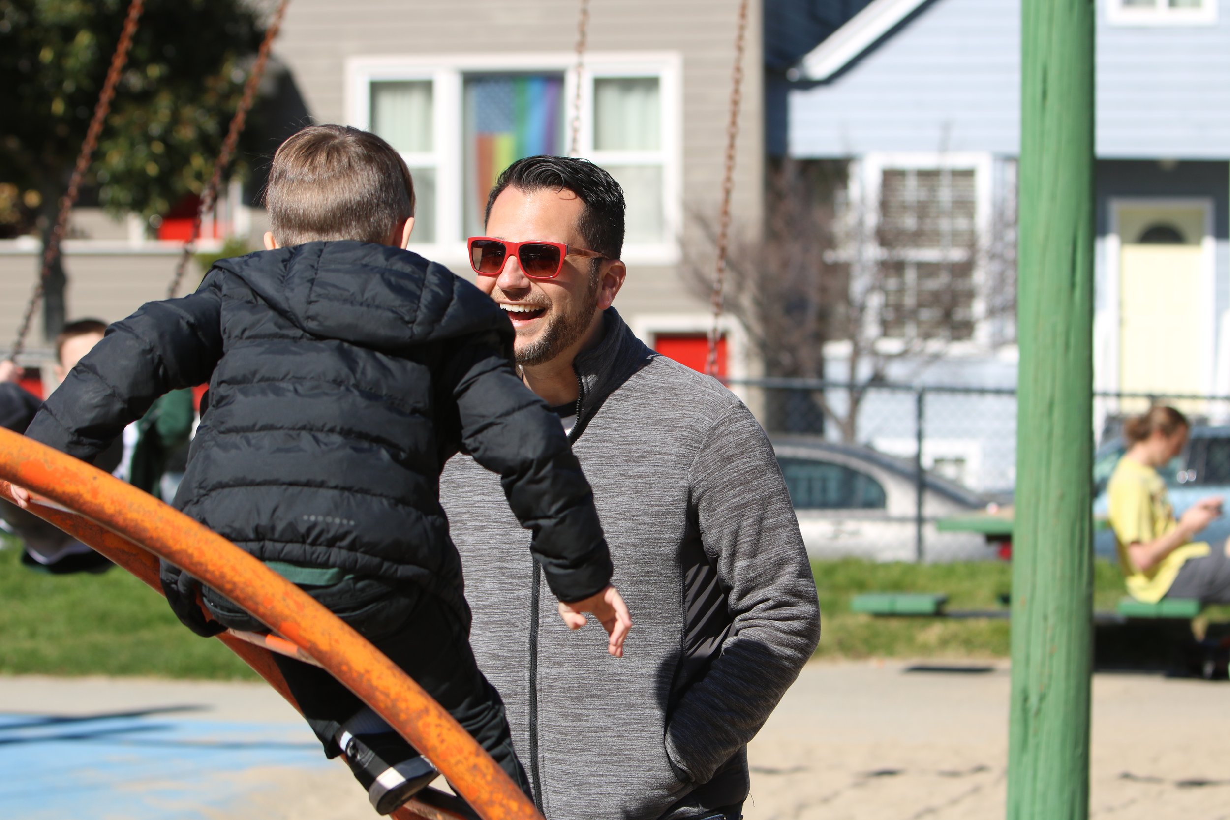 Ryan smiling and talking to a child on a playground with swings and a house in the background.