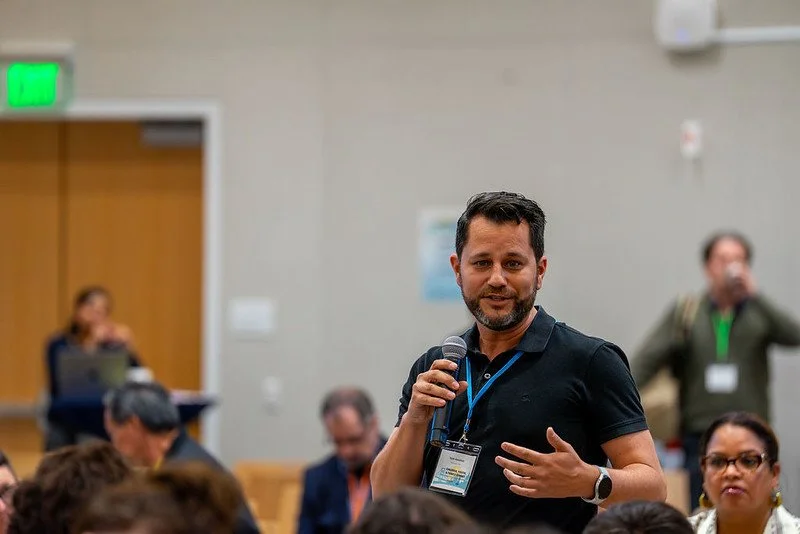 Ryan holding a microphone and speaking at a conference in a room with child and family advocates and leaders.