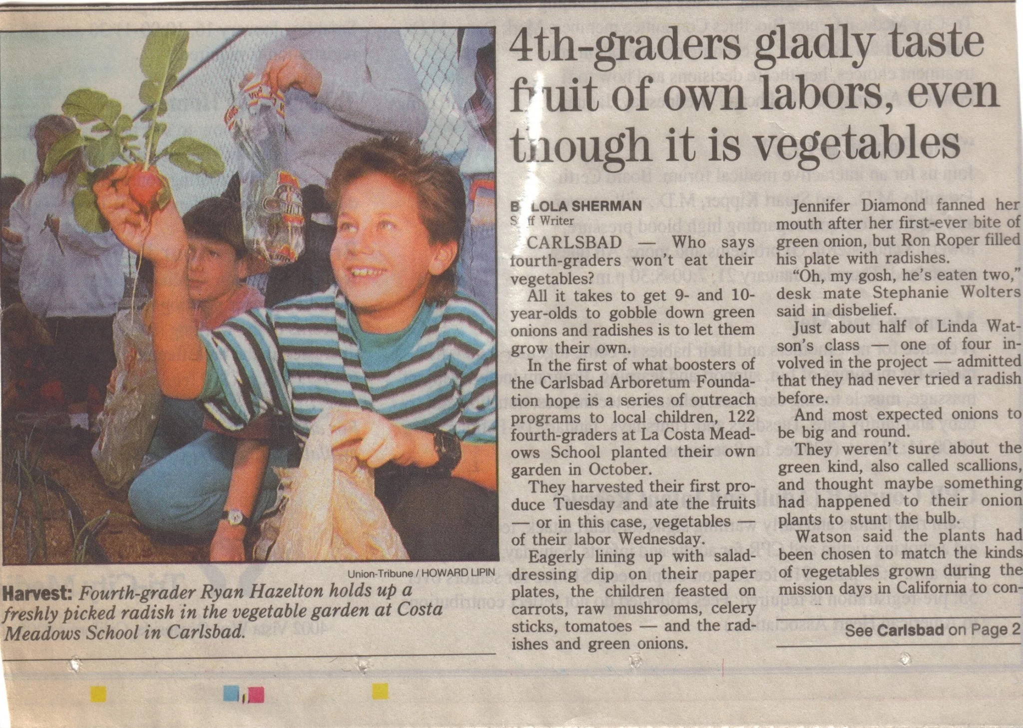 Picture of a news article featuring Ryan holding a freshly picked radish, in a vegetable garden at La Costa Meadows School in Carlsbad.