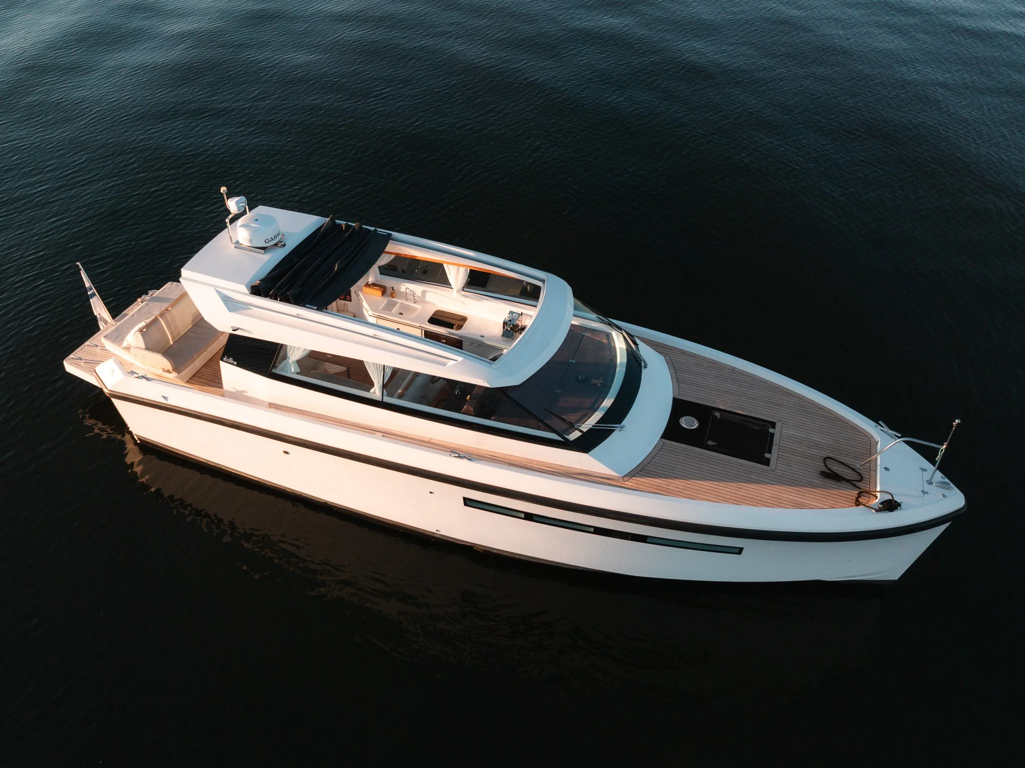 A white yacht with a black canopy and wooden deck floating on dark blue water.