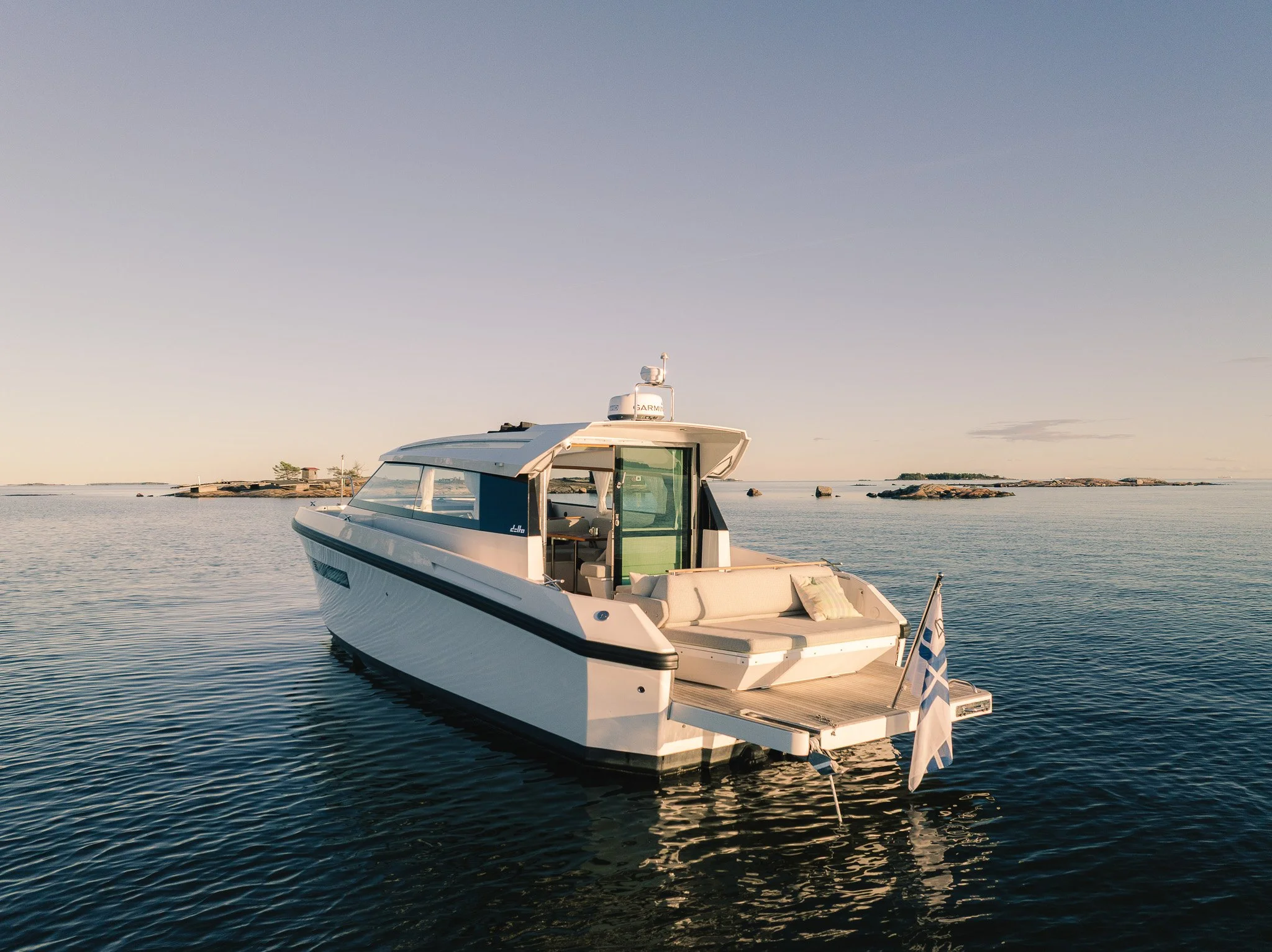 A white yacht floating on calm water, with a rocky shoreline in the background during sunset or sunrise.