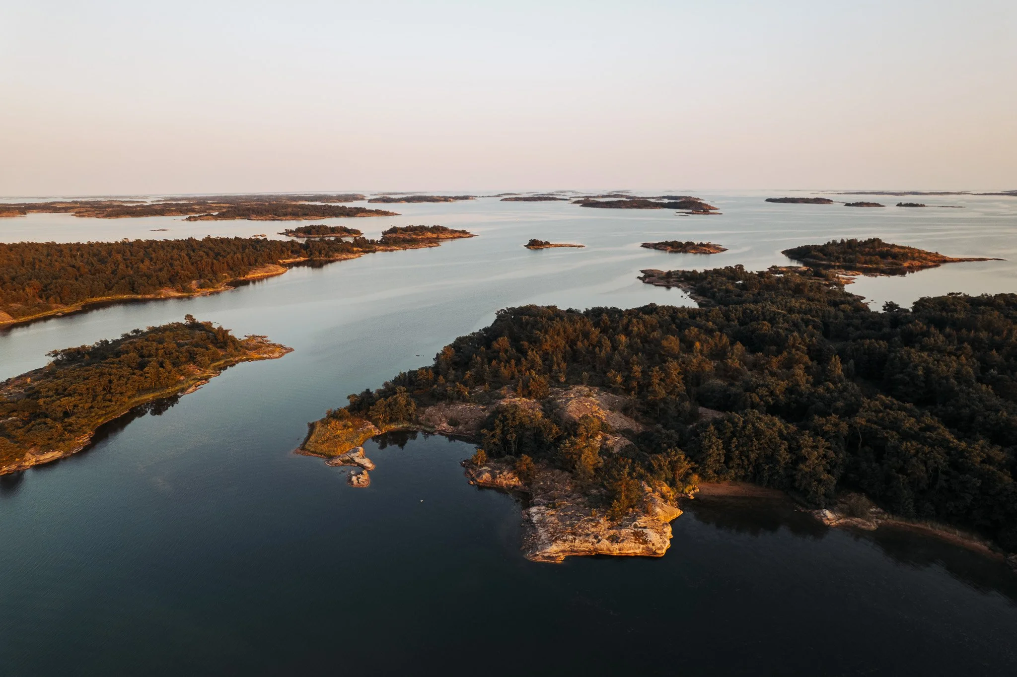 Aerial view of a landscape with numerous small islands and peninsulas covered in trees, surrounded by calm water during sunset.