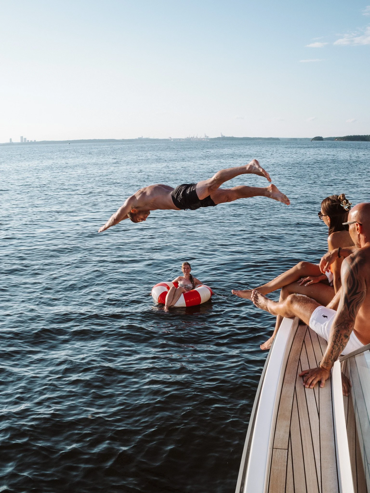 A man diving off a boat into a body of water with other people watching on the boat.