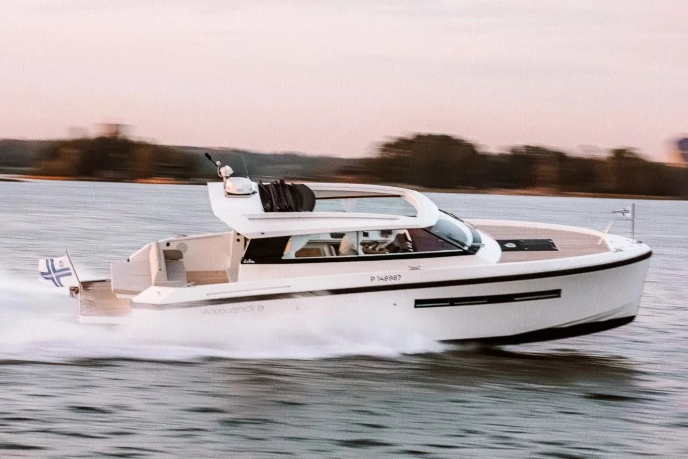 A white motor yacht named Nexanora cruising on the water at sunset.