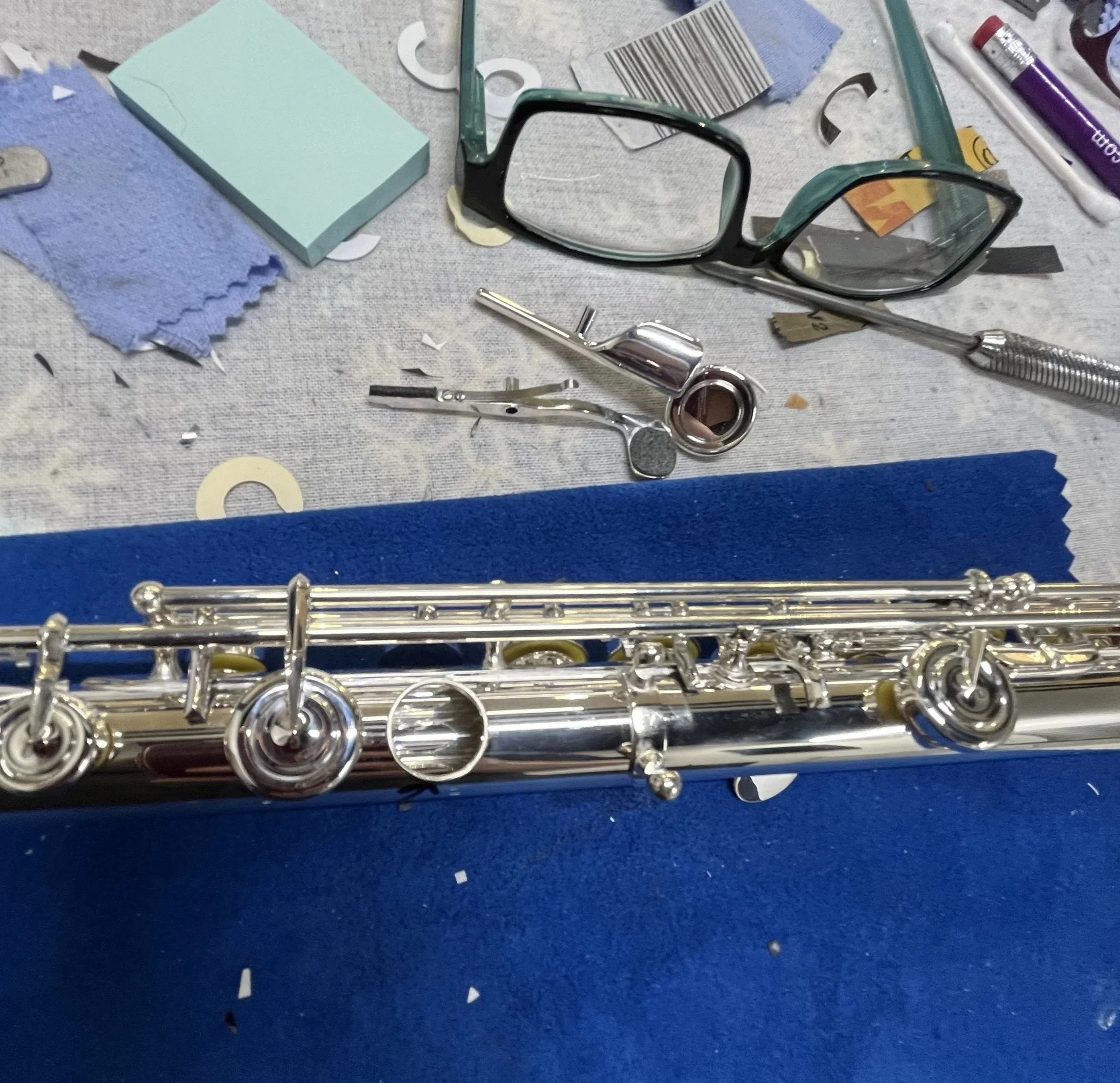 Disassembled glasses, surgical tools, and paper scraps on a work surface, with a blue cloth and paper towels nearby.