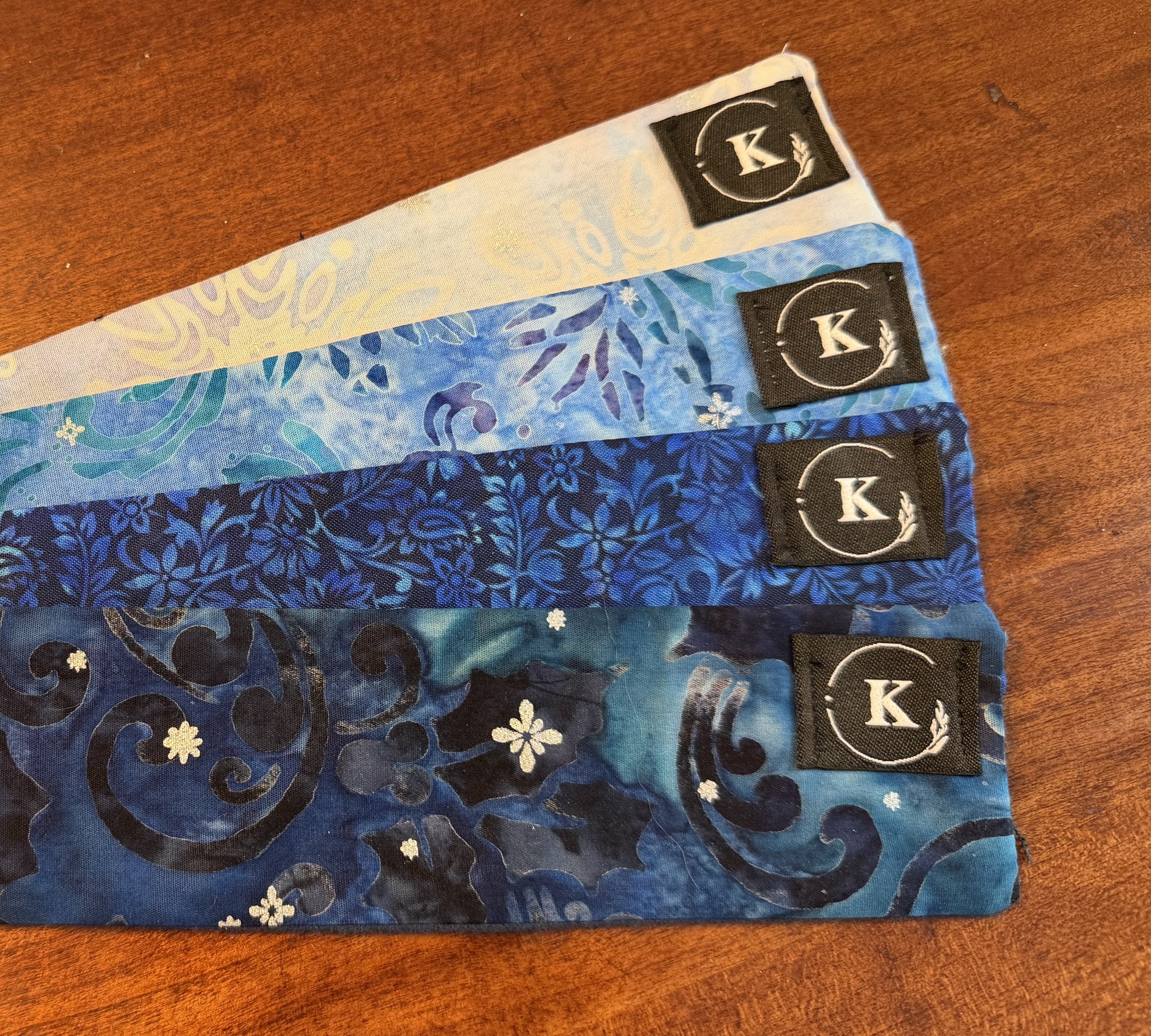 Three fabric face masks with different blue and white snowflake patterns, placed on a wooden surface.