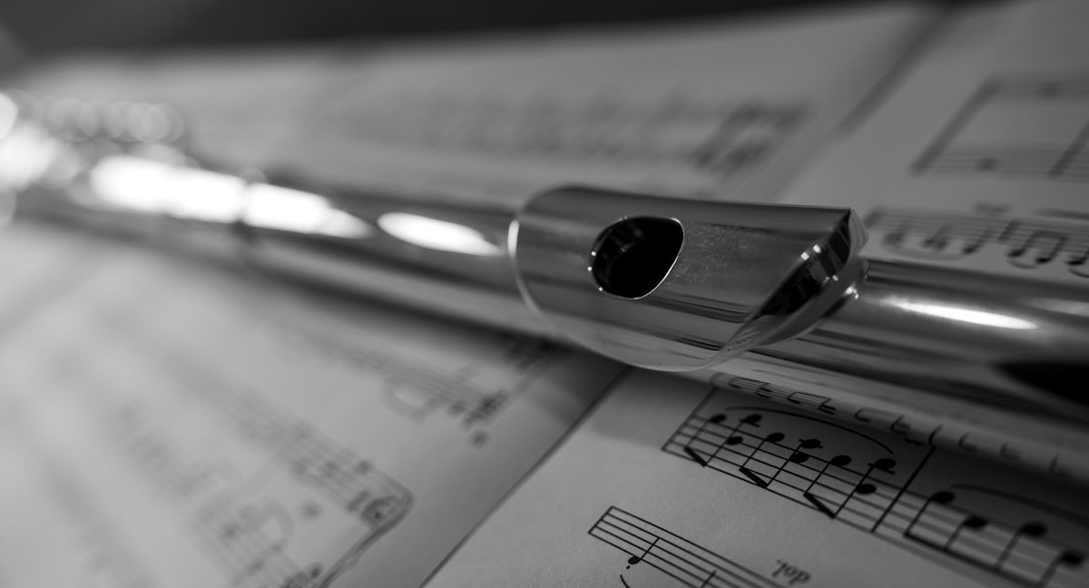 Close-up of a metallic baton resting on sheet music with musical notes, in black and white.