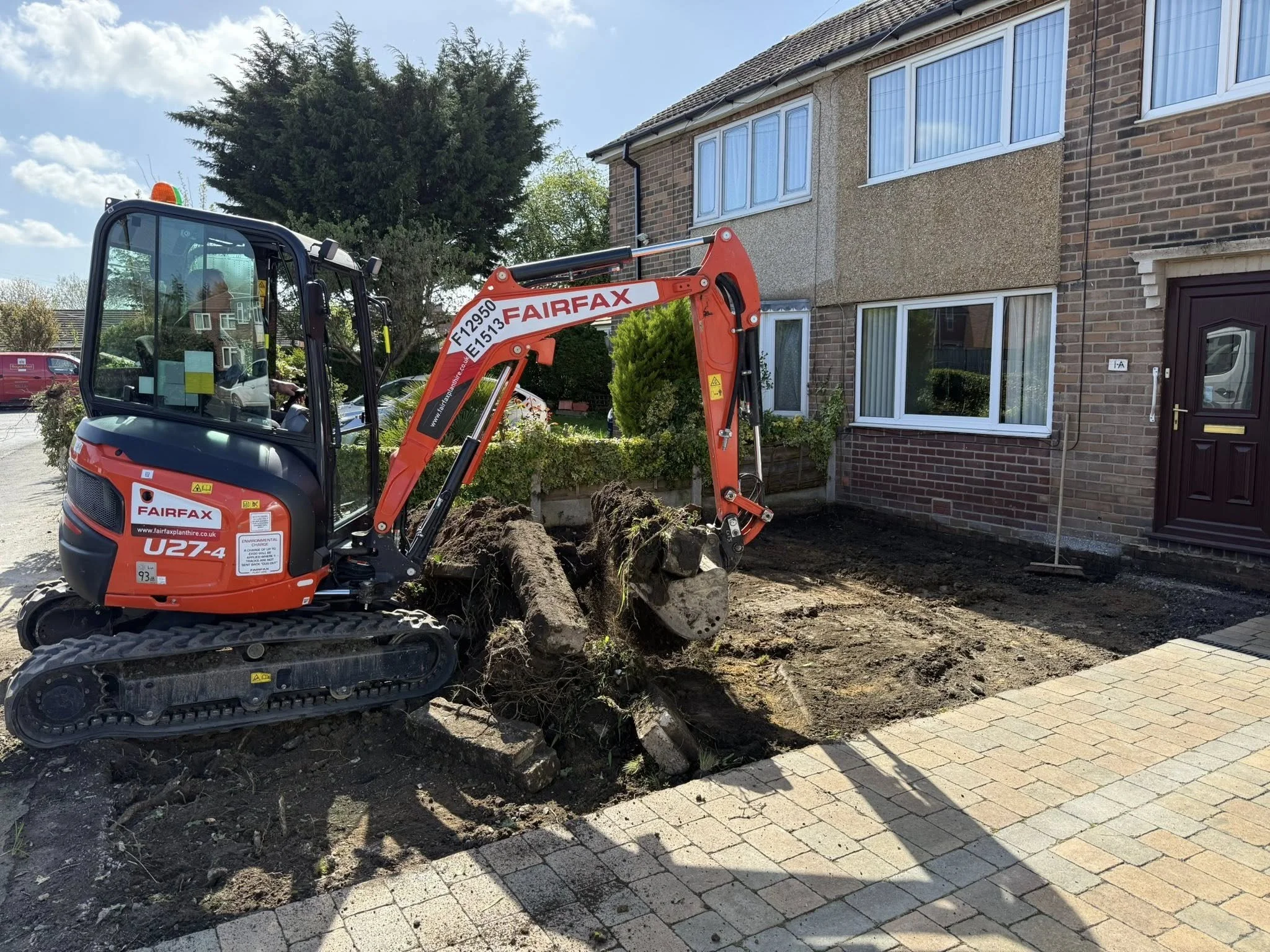 Groundworks using a digger to prepare the ground for driveway extension at the front of a residential property. Earth clearing and landscaping.