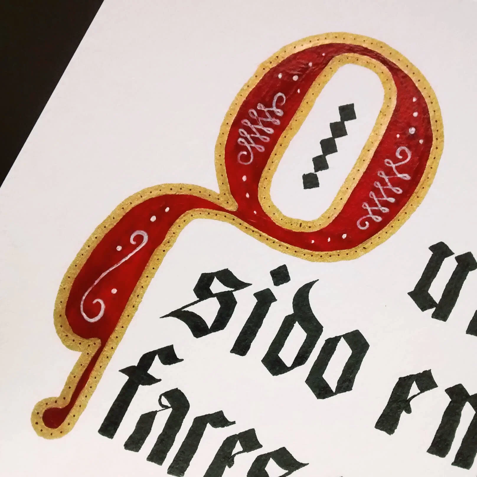 Close-up of a tattoo-style illustration featuring a red and gold ribbon with white decorative details, and black Gothic script text underneath.