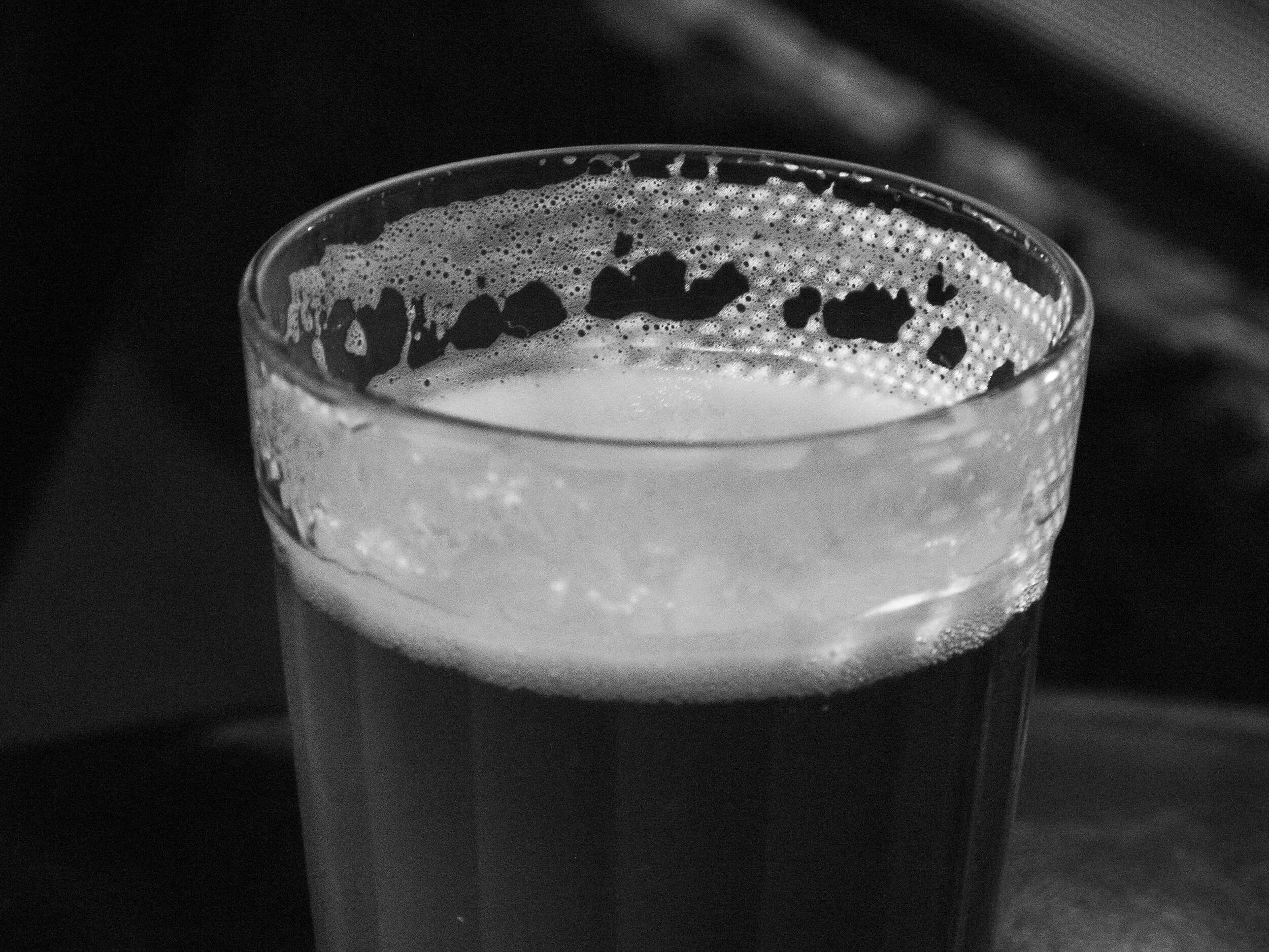 Close-up of a glass filled with a foamy beverage, possibly beer, with bubbles visible on the surface, against a dark background.