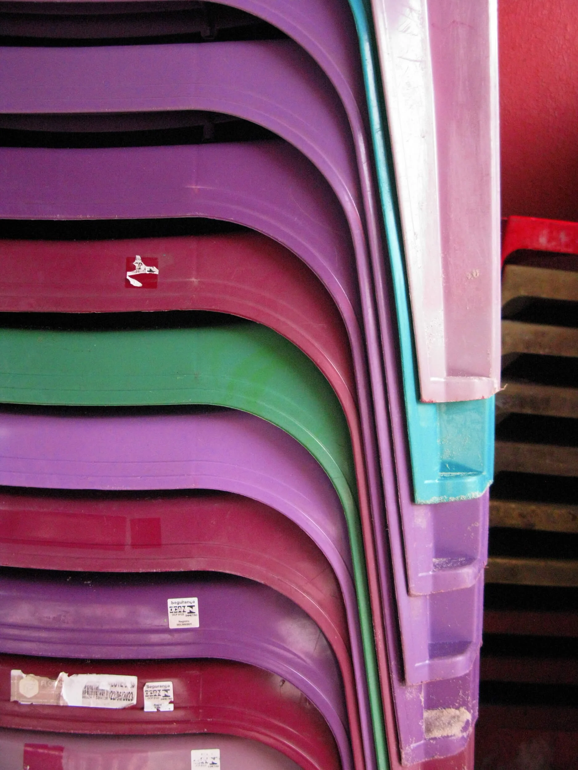 Stack of colorful plastic chairs in purple, red, and green, placed against a red wall.