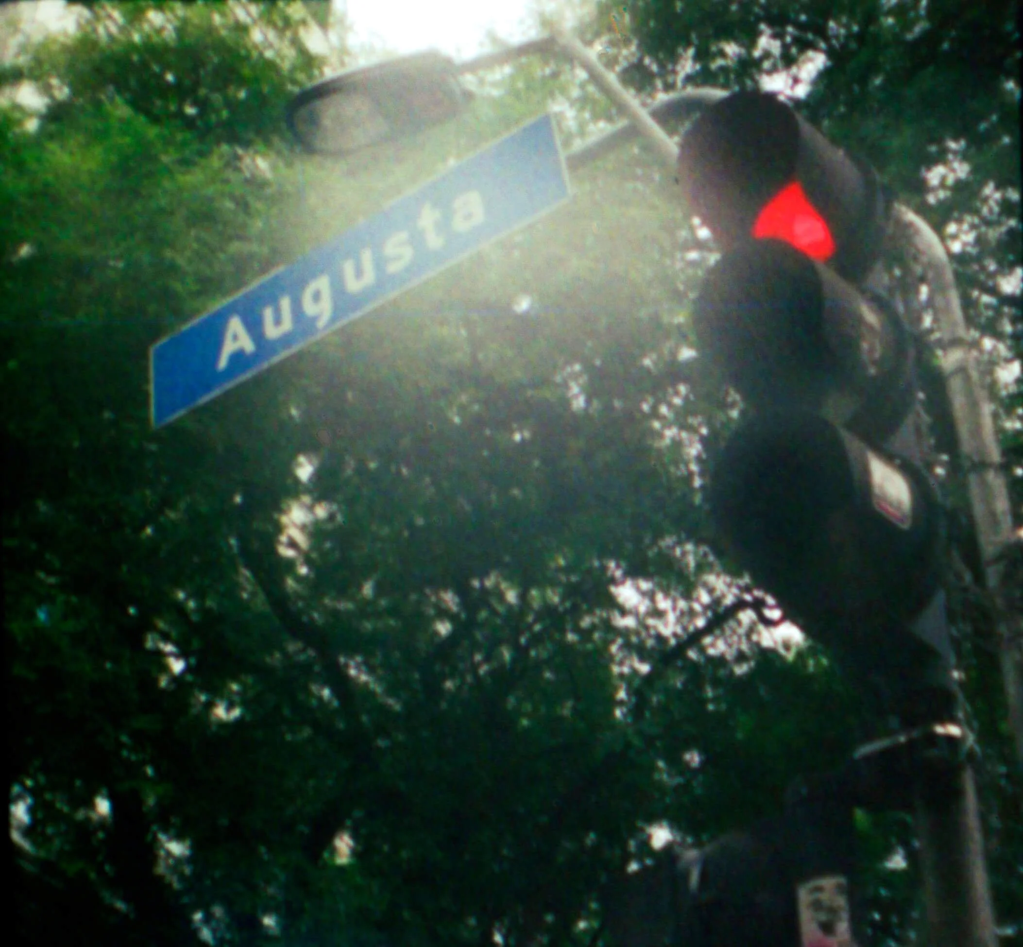 Street sign that reads "AUGUSTA" with trees in the background and a person walking.