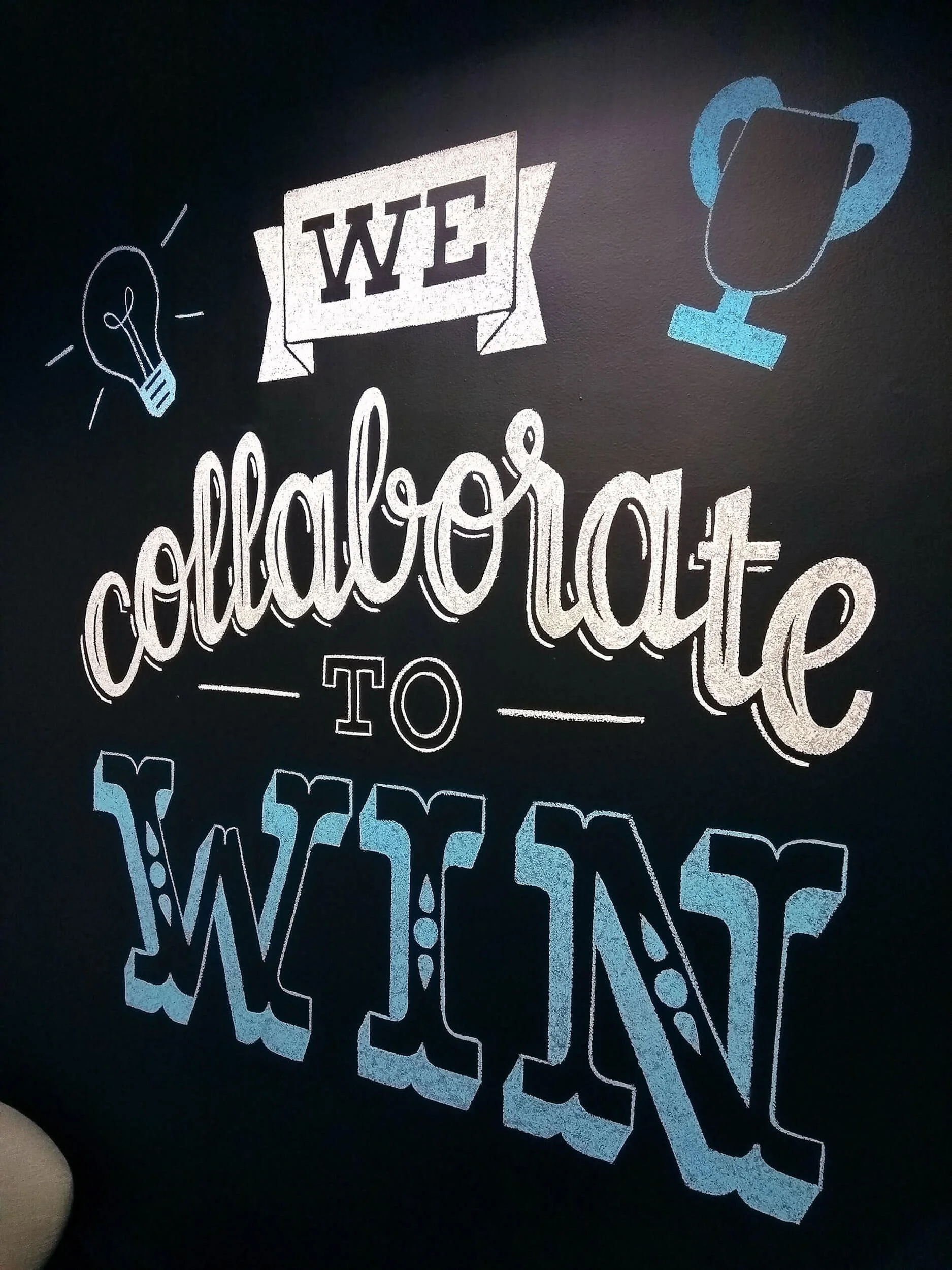 A black chalkboard-style sign with colorful chalk writing and illustrations, including a light bulb, the word 'ween' in a banner, a trophy, and various numbers and symbols, promoting a coffee sale.