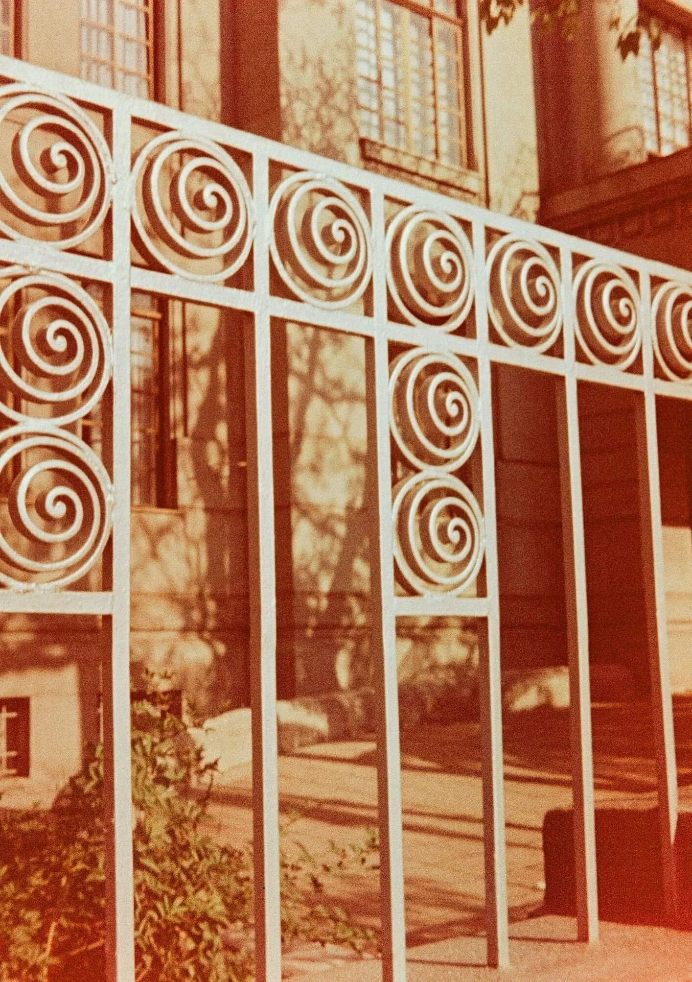 White decorative metal fence with spiral patterns in front of a house with large windows and brick exterior.