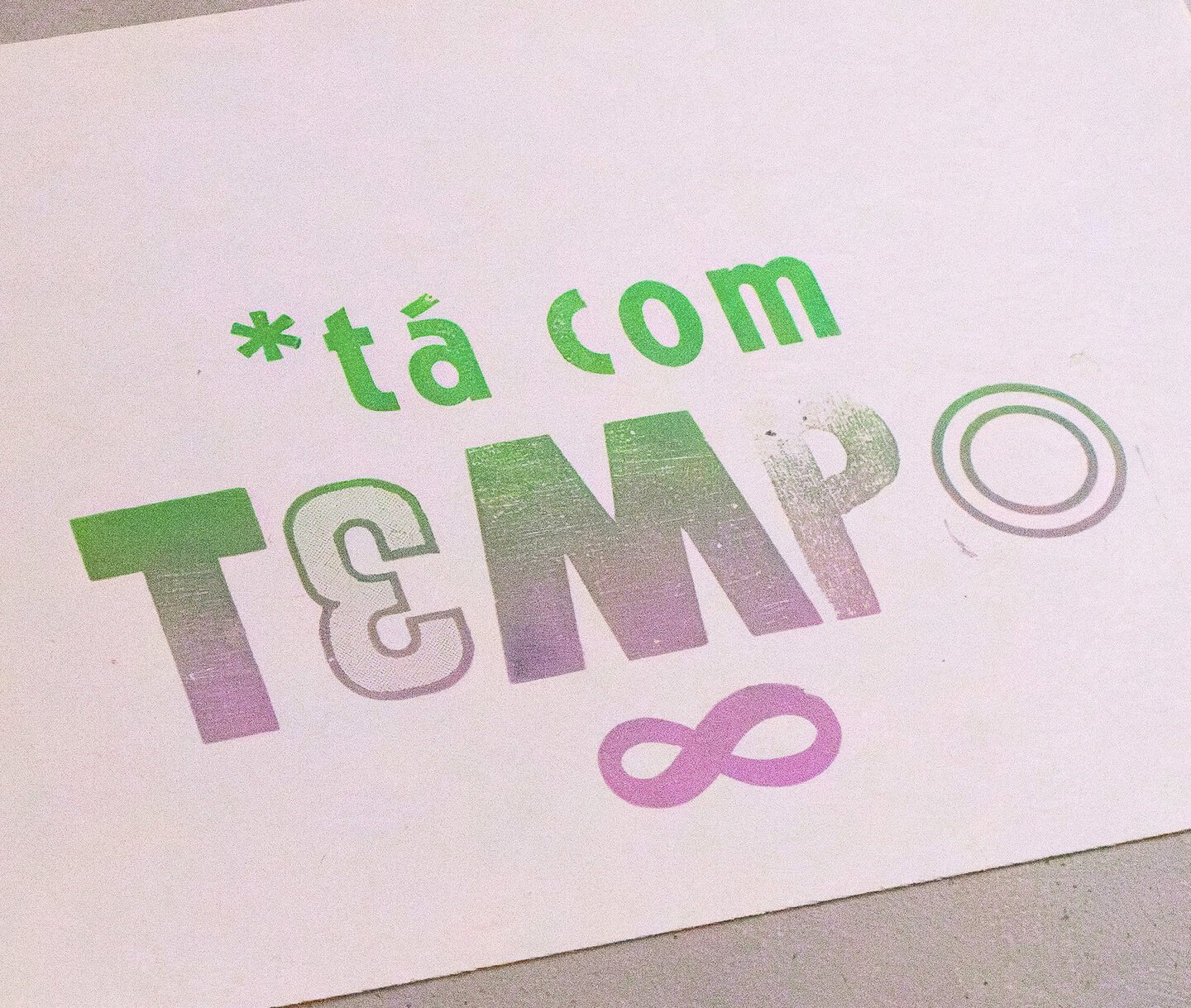 Colorful printed paper with the phrase '*tá com T&N' and an number 3 in outline, a pink infinity symbol, and a circle outline on white background.