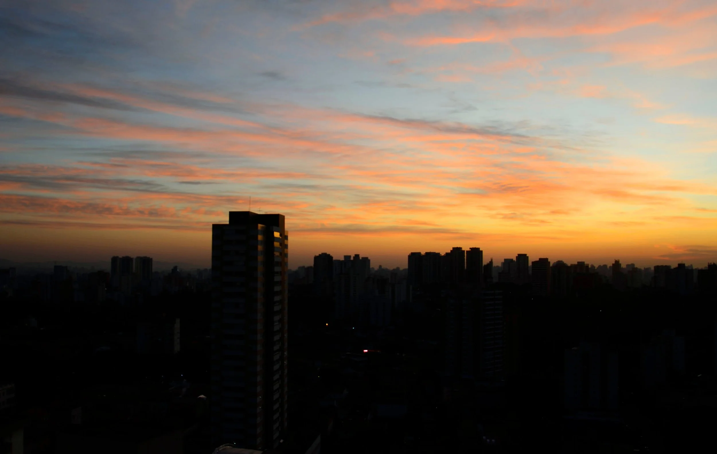 City skyline during sunset with colorful clouds in the sky and darkened buildings in the foreground.