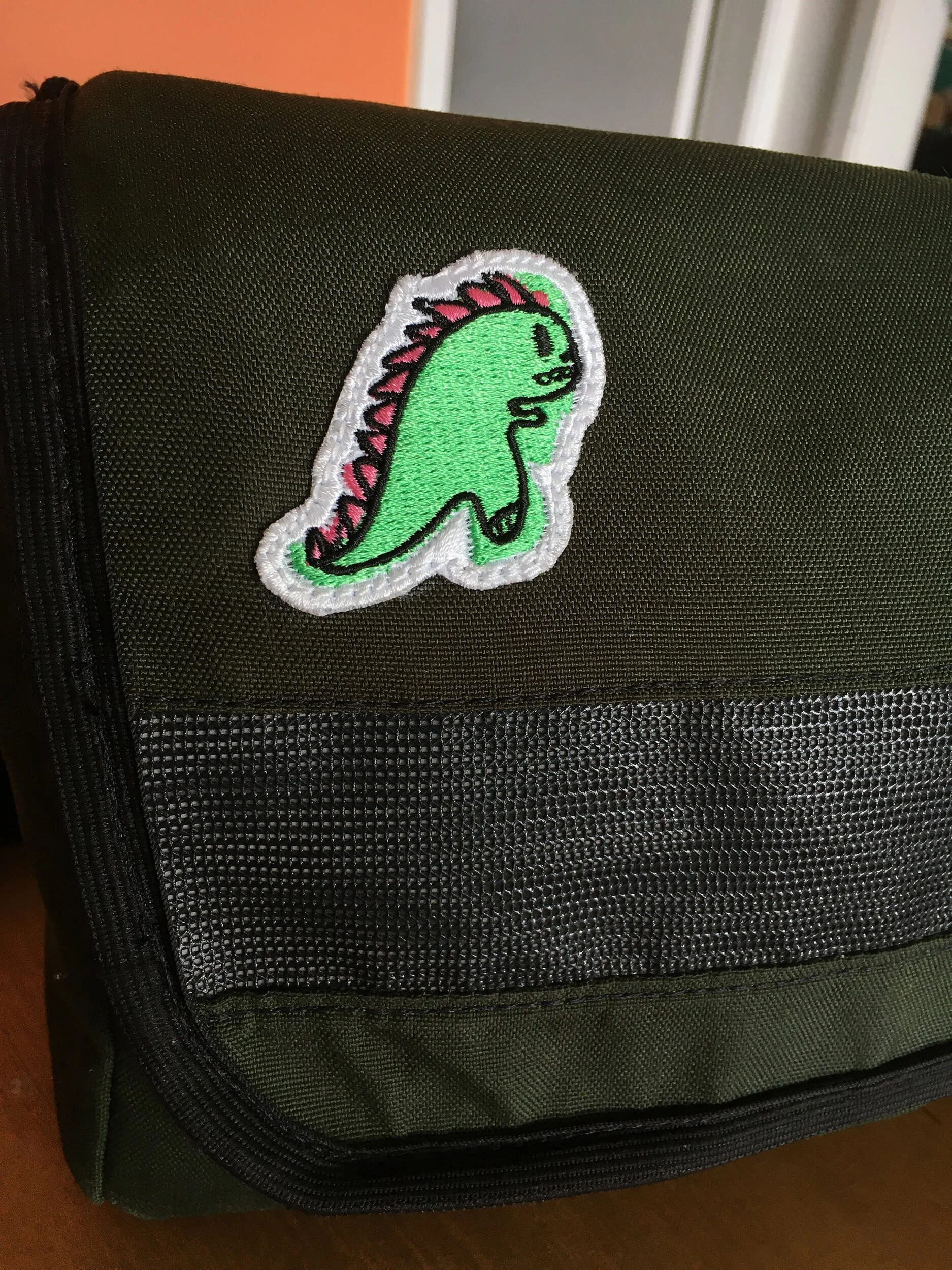 Green backpack with a dinosaur patch on the front pocket