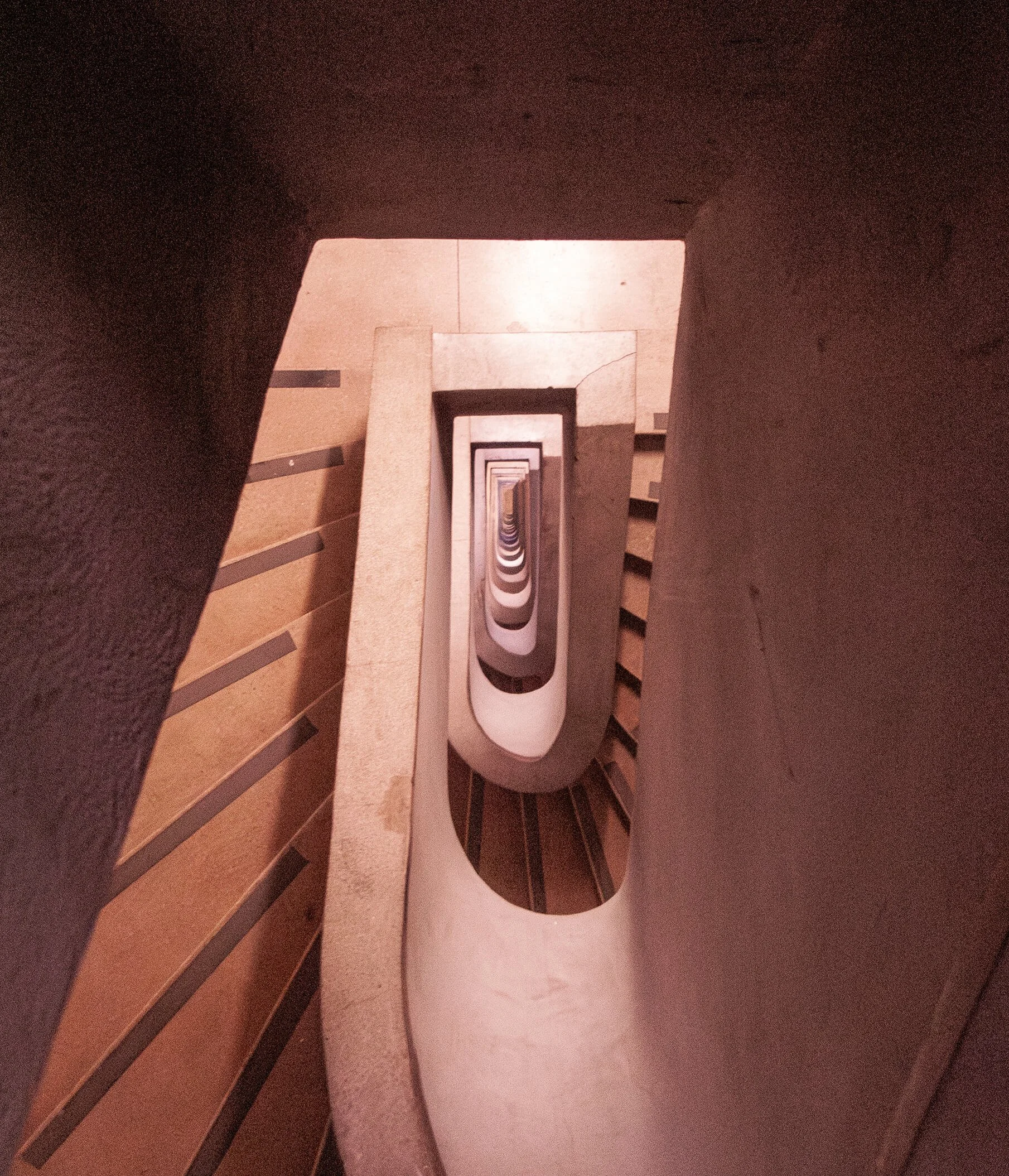 Looking down a stairwell with rectangular steps and a railing, showing a repeating pattern of stairs.